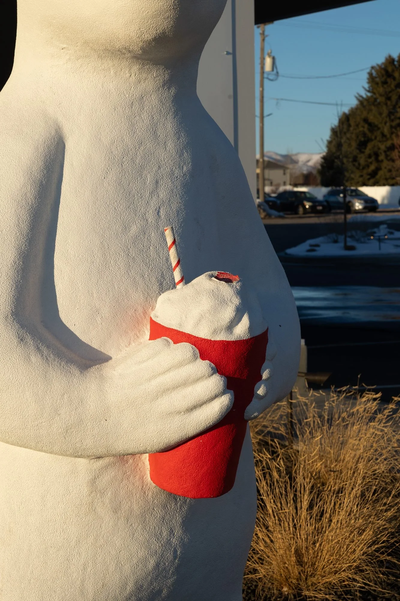 A white polar bear statue holding a red shake cup outdoors in winter sun