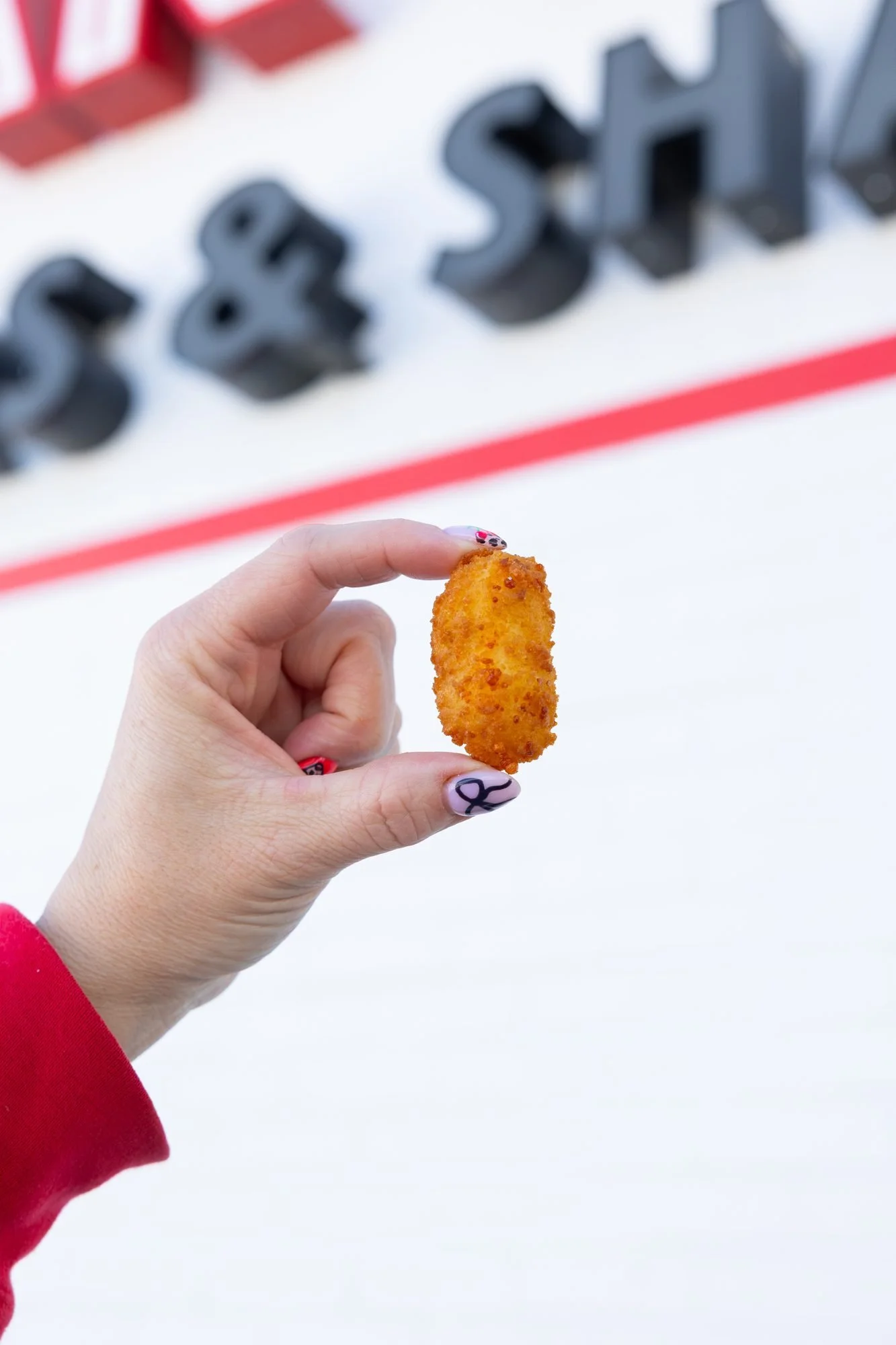 A hand holding a fried cheese curd in front of the Polar Bear sign on the building