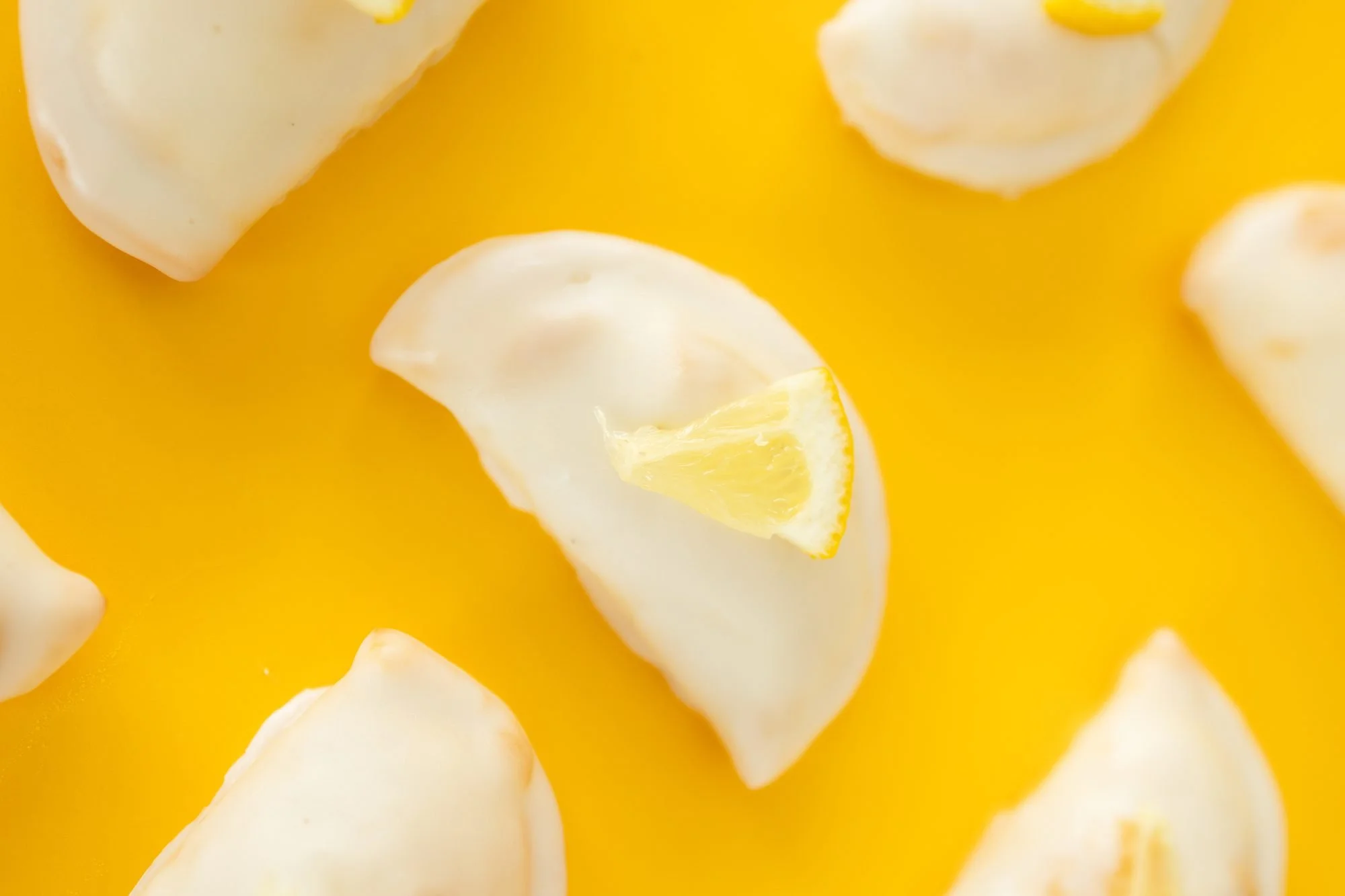Close view of glazed hand pies topped with lemon wedges on a yellow background