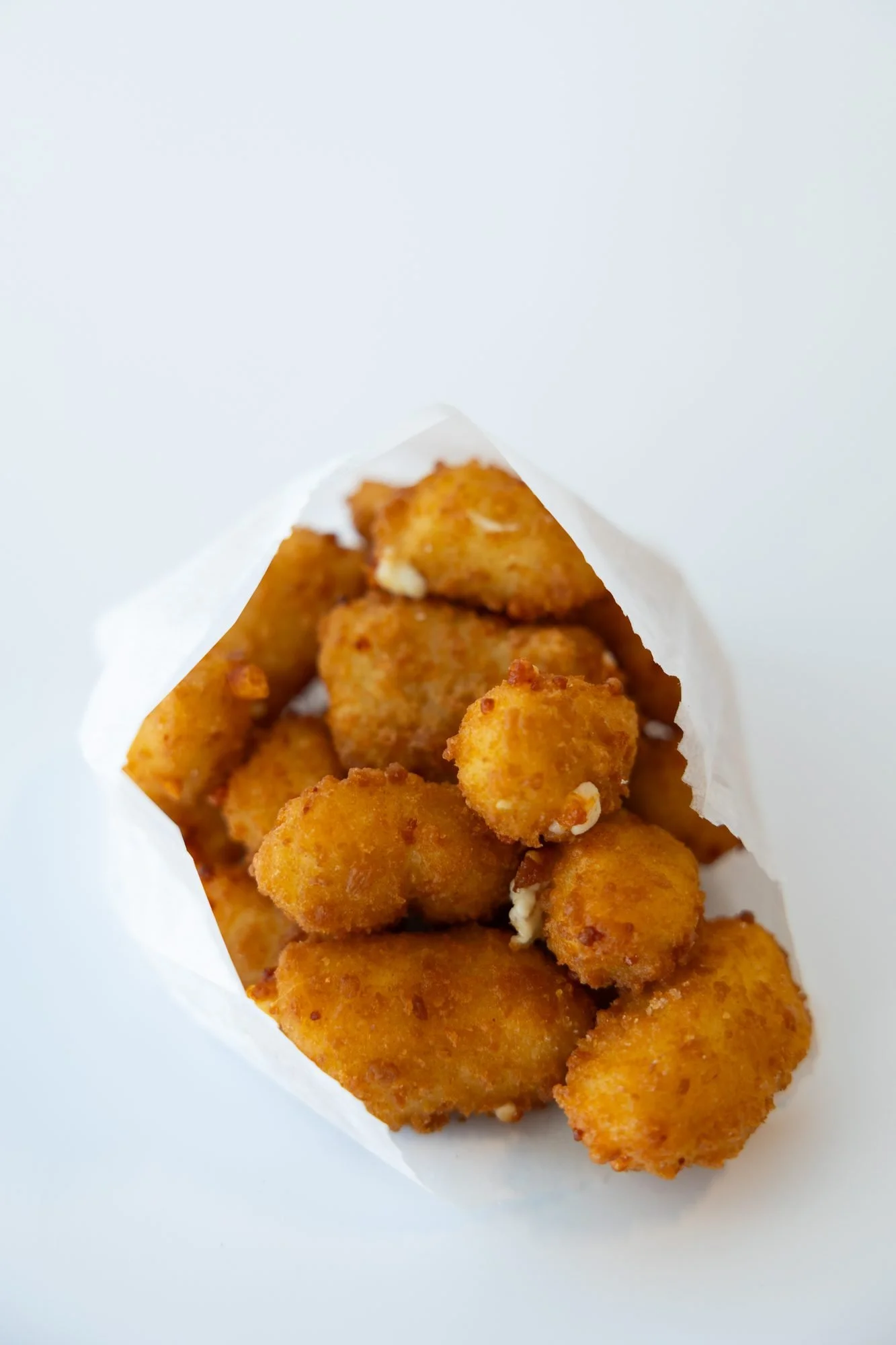A paper sleeve of golden fried cheese curds on a white background