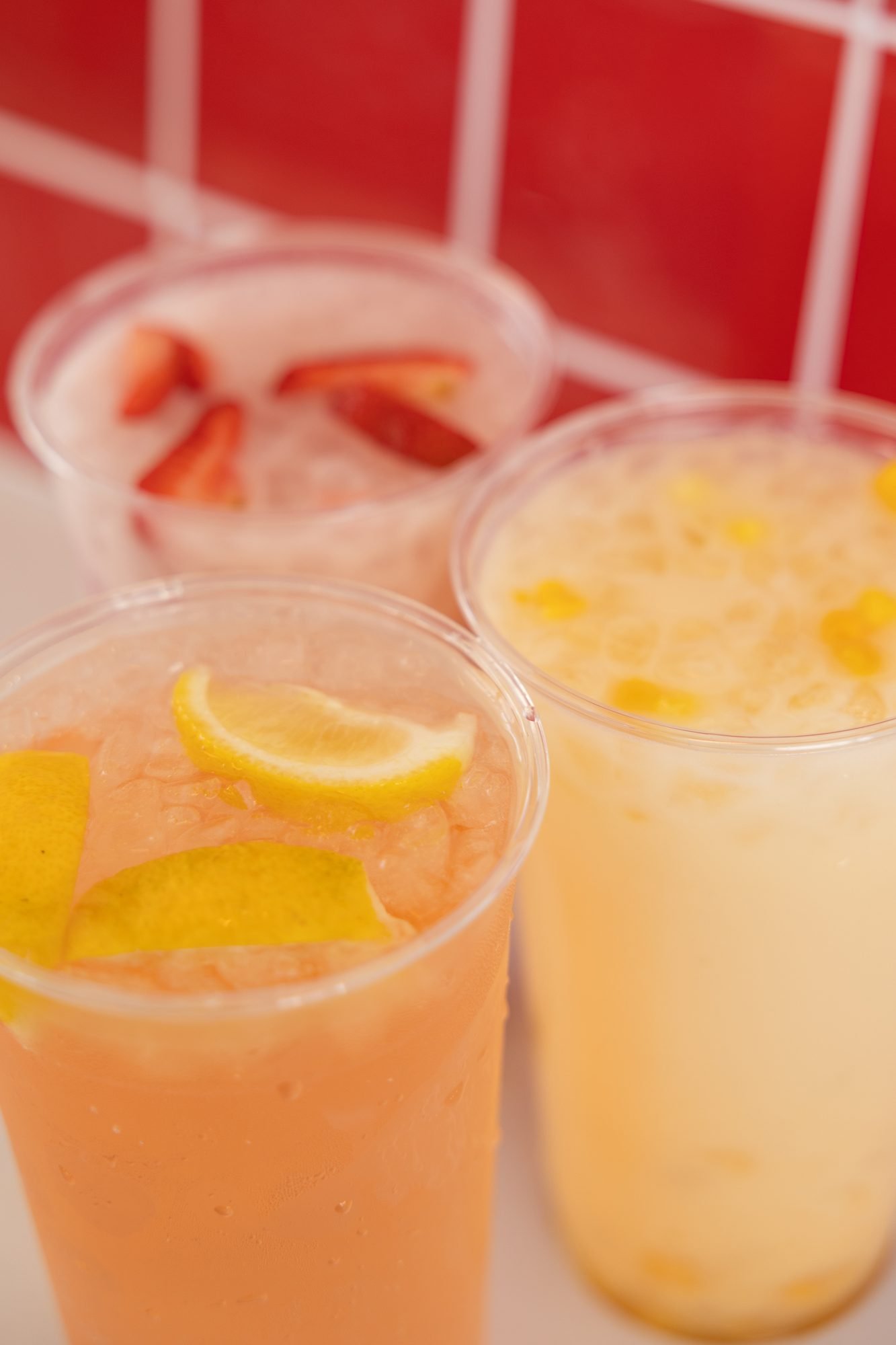 Two iced lemonades with lemon slices in front of a red tile wall