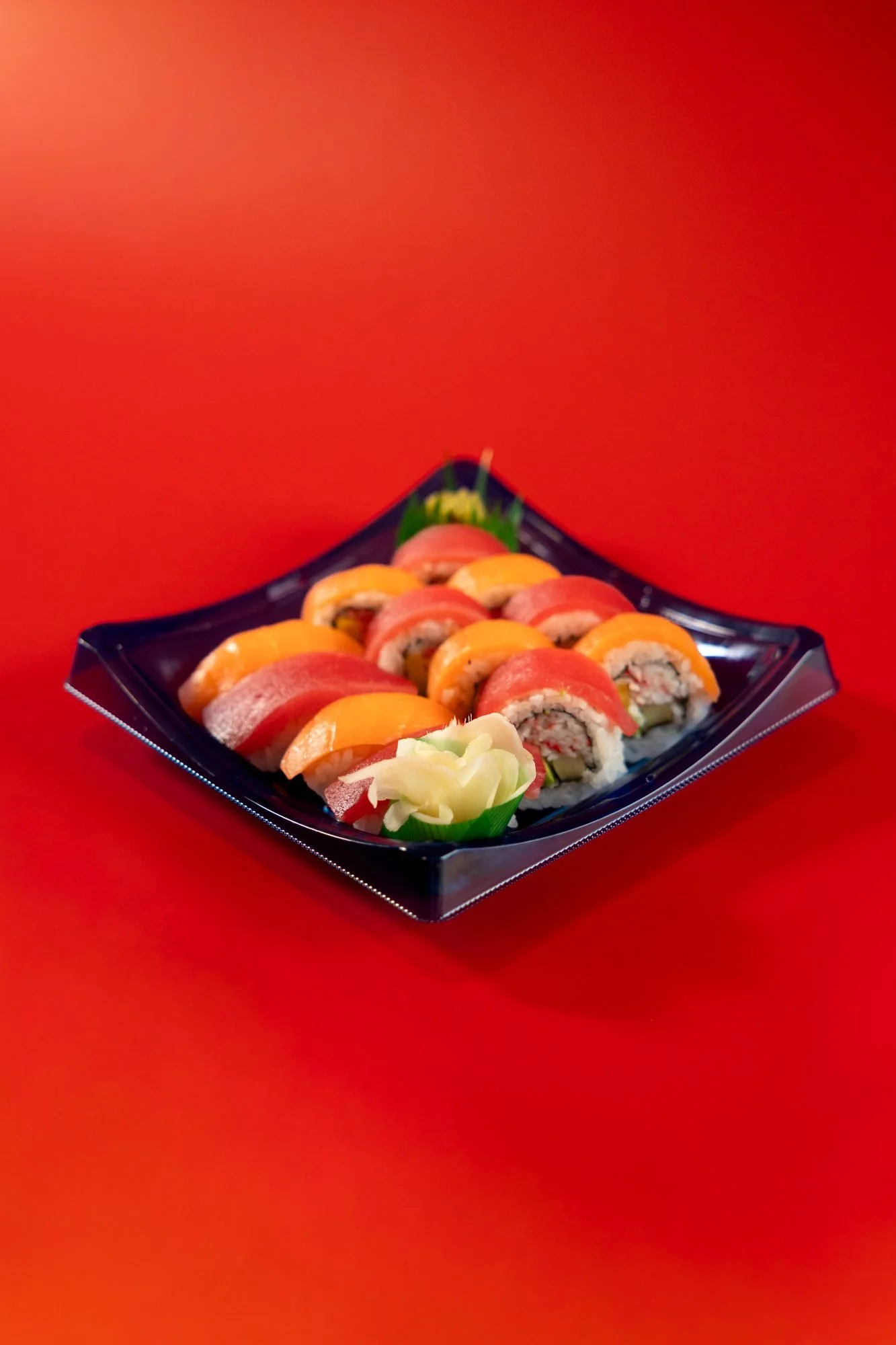 A tray of rainbow sushi rolls with pickled ginger on a red background