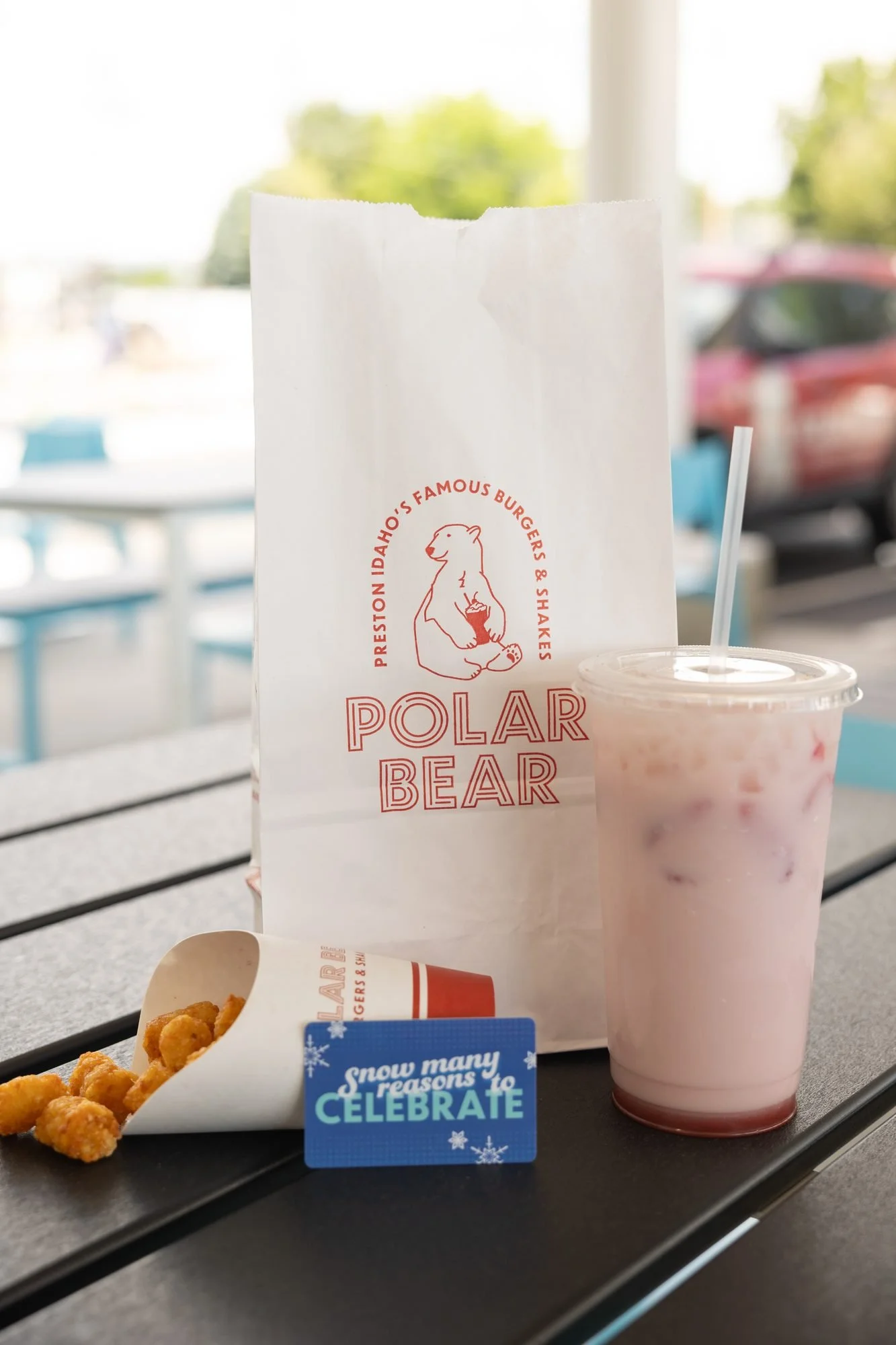 A Polar Bear takeout bag and a pink drink on an outdoor table