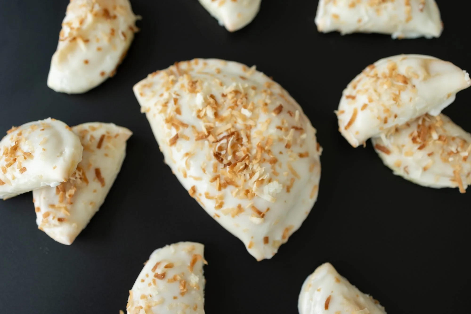White glazed hand pies sprinkled with toasted coconut on a black surface