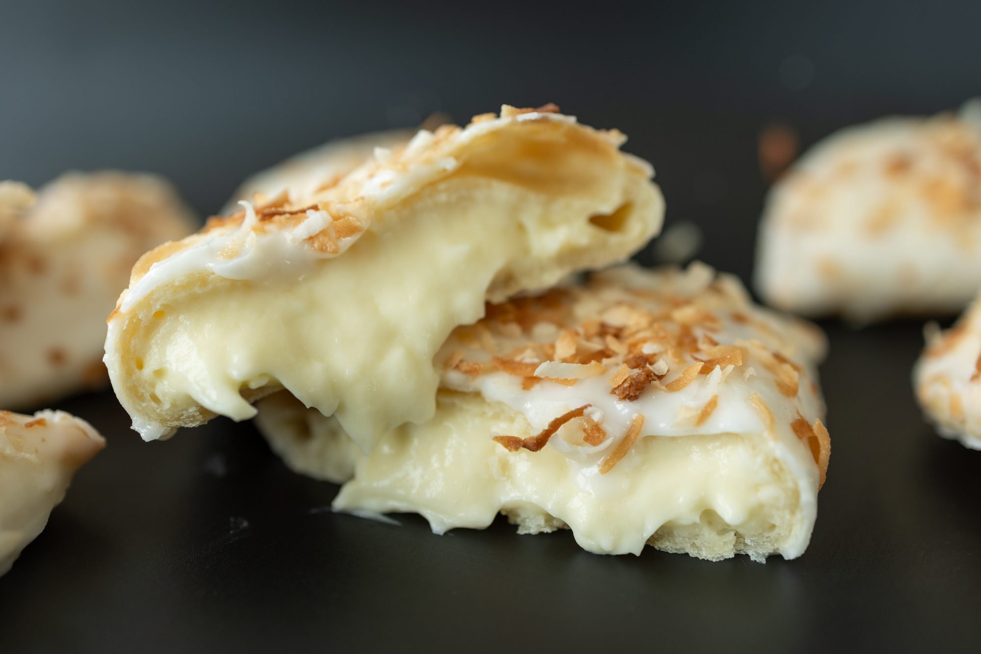 A white glazed coconut hand pie broken open to show a creamy filling on a black surface