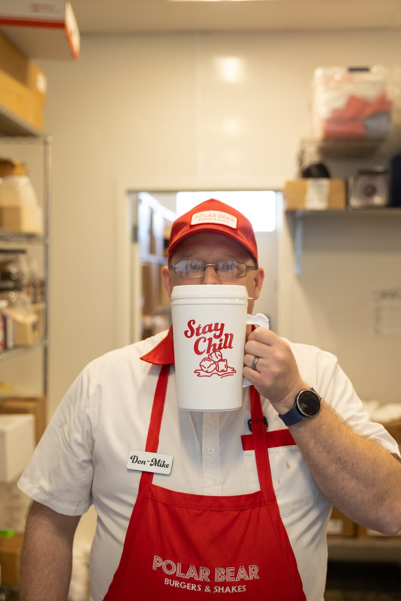 A Polar Bear employee in an apron holding a Stay Chill mug in the kitchen