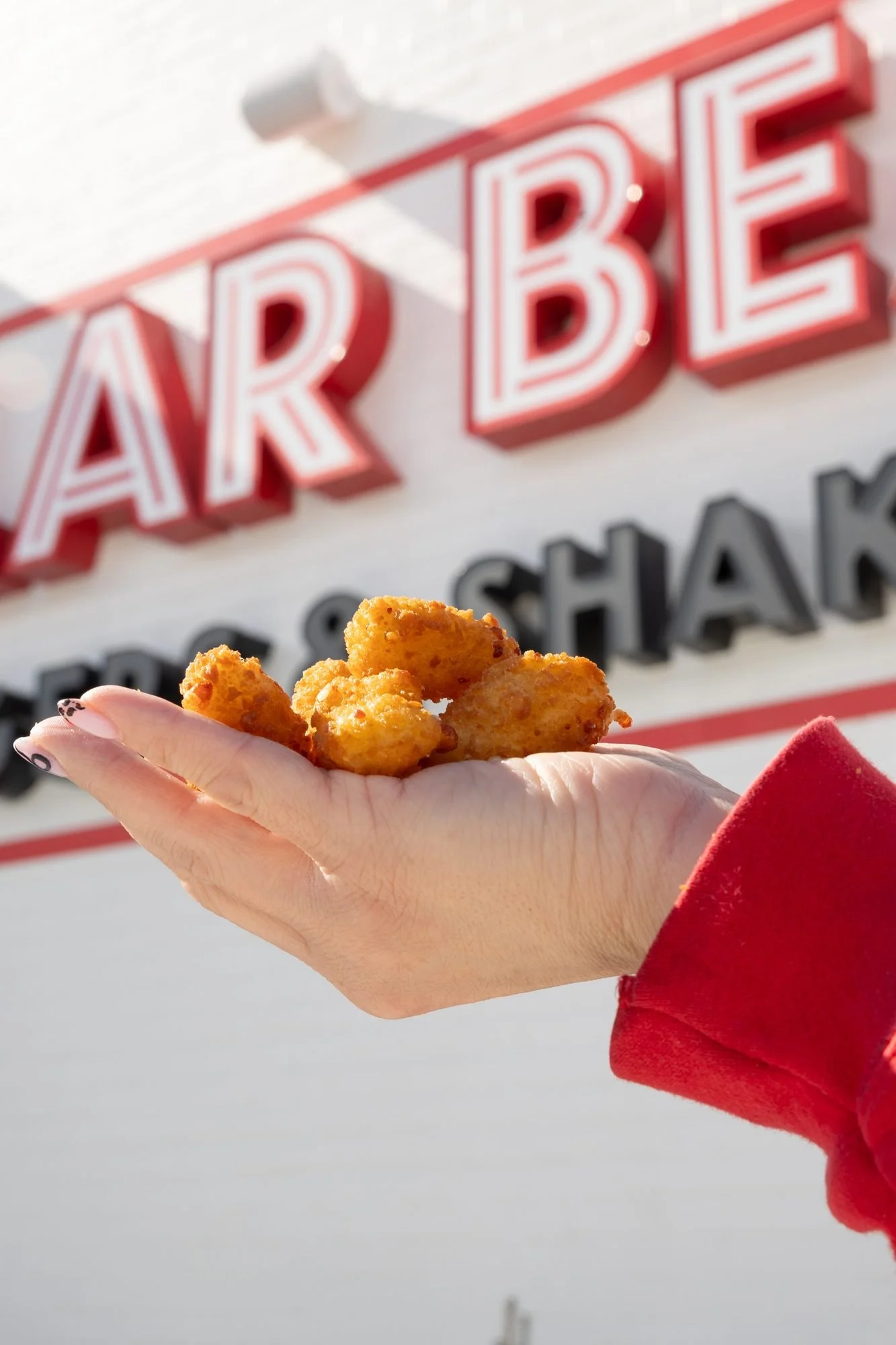 A hand holding fried cheese curds in front of the red Polar Bear sign