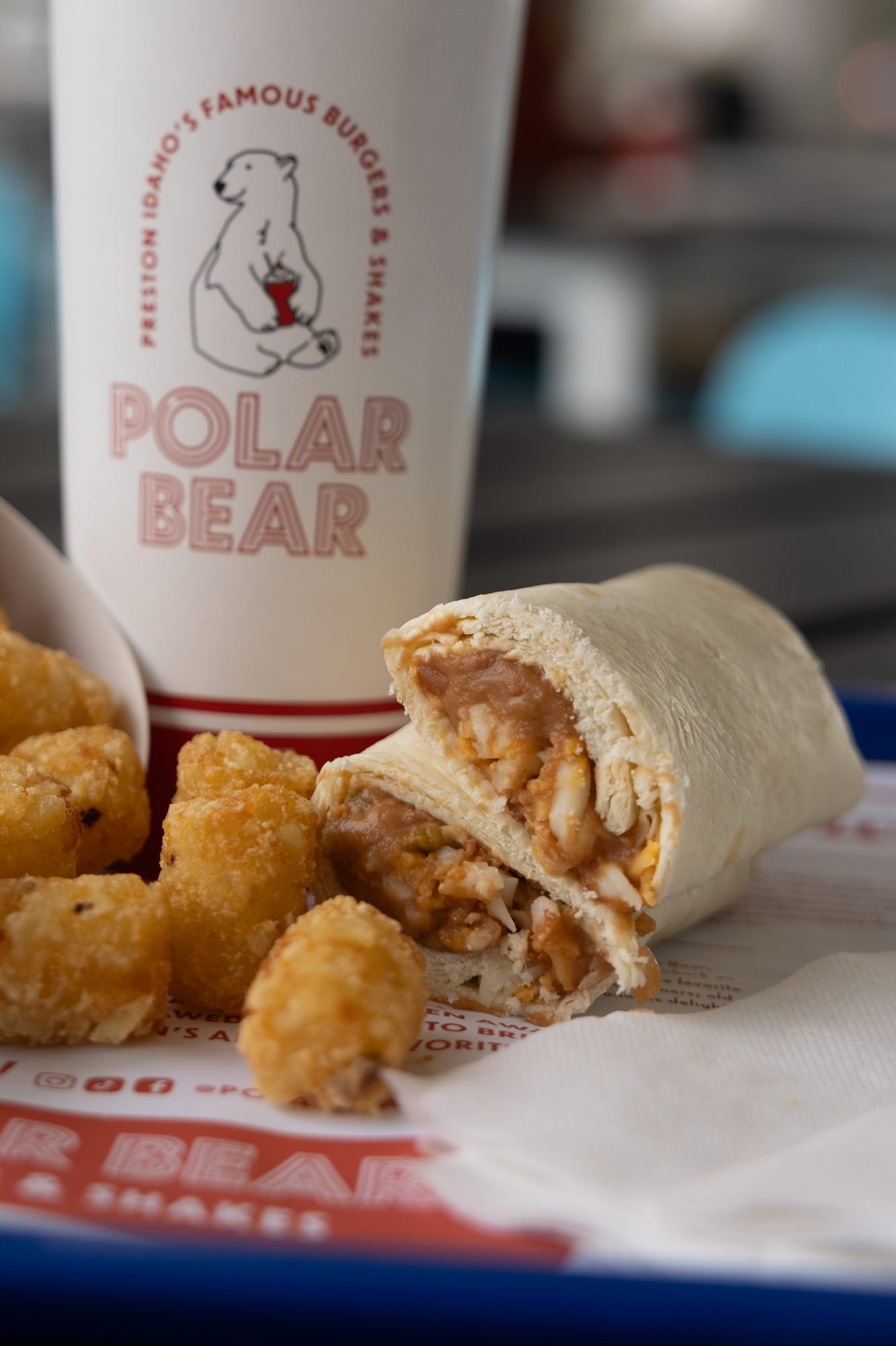 A Polar Bear drink, tater tots and a halved wrap on a branded tray liner