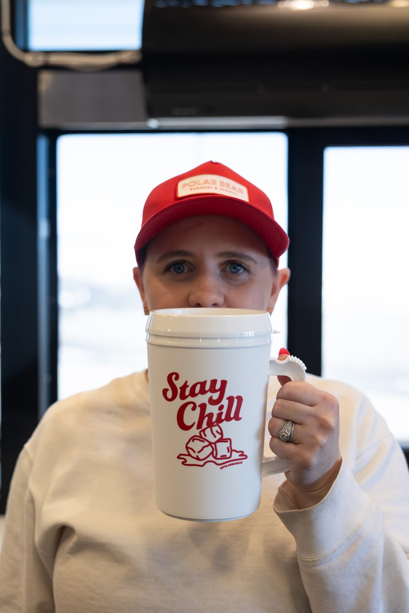 A woman in a red Polar Bear cap holding a Stay Chill mug by a window