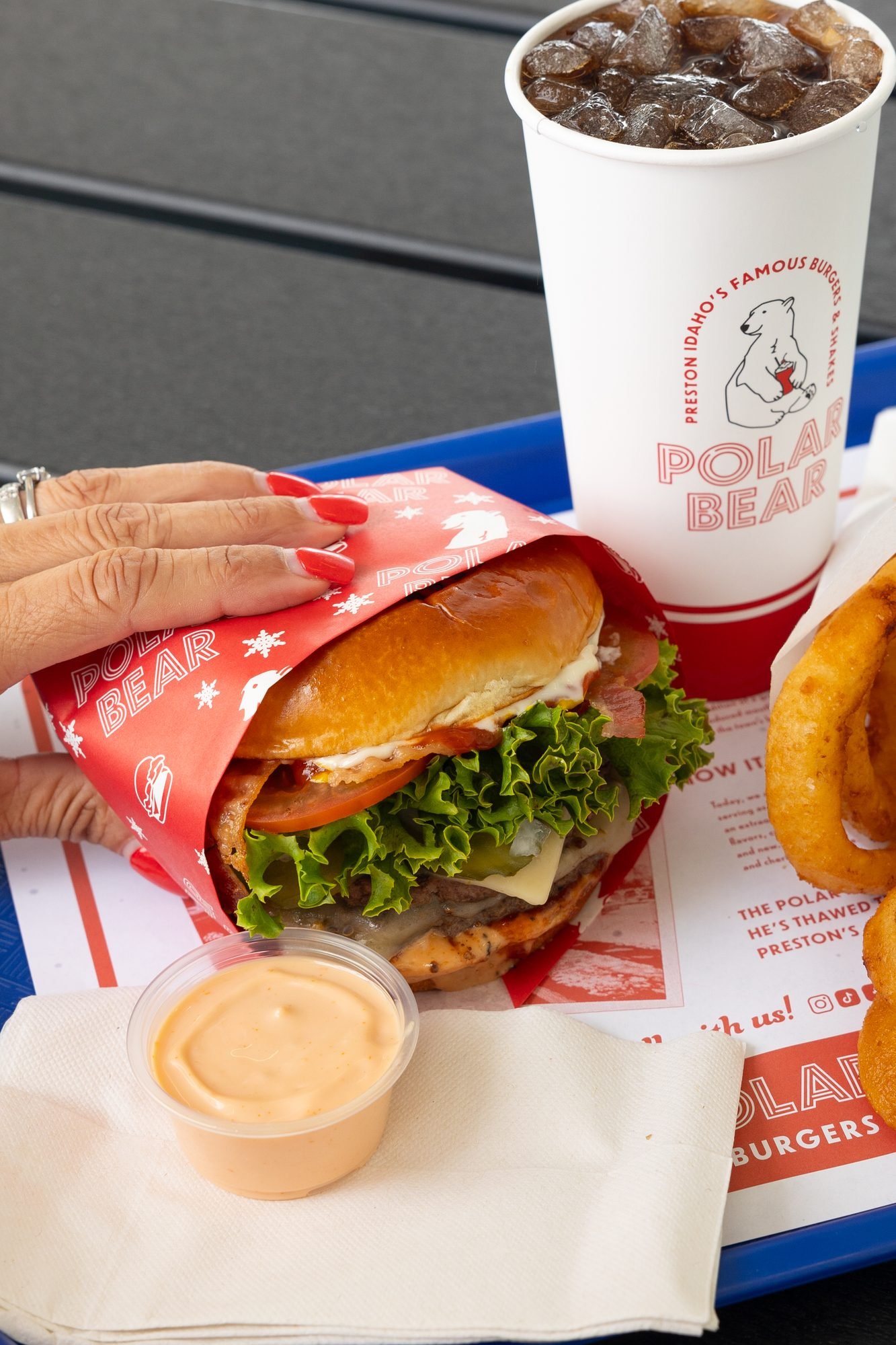 Hands unwrapping a burger on a Polar Bear tray with a drink and dipping sauce