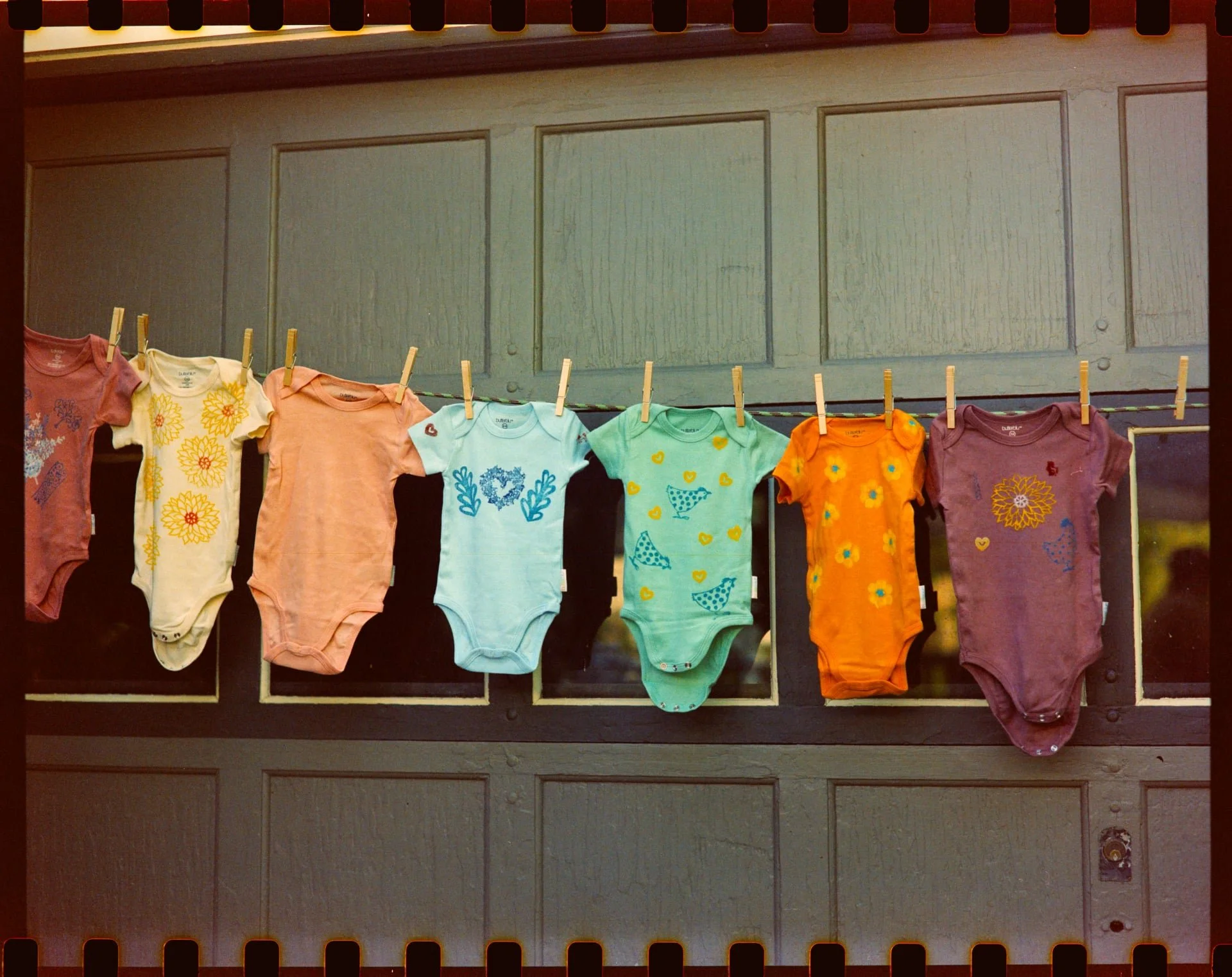 Colorful children's t-shirts hanging on a clothesline with clothespins, displayed against a wooden background.