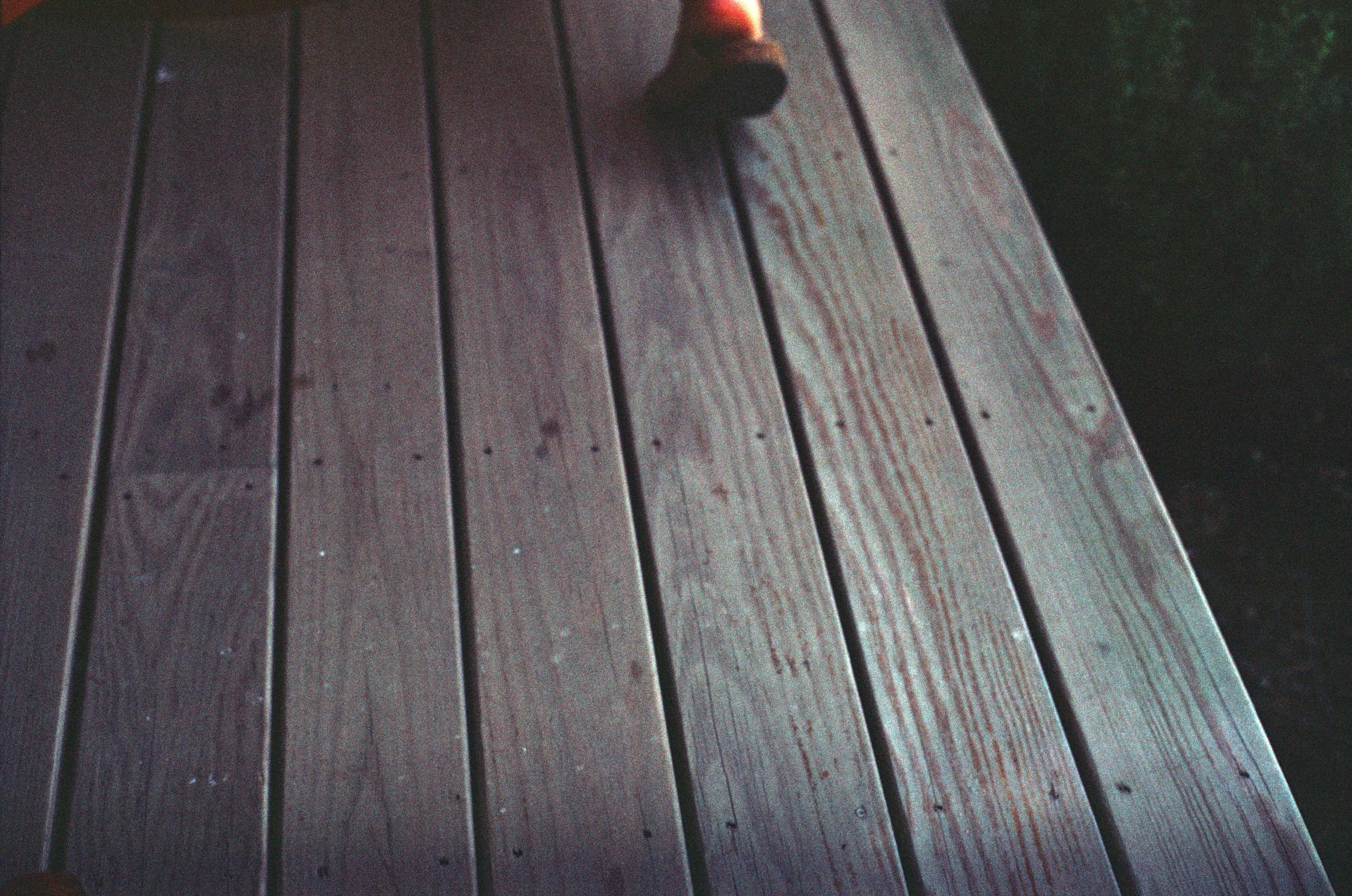 Close-up of wooden planks on a deck with a person's foot wearing a sandal visible at the top edge.