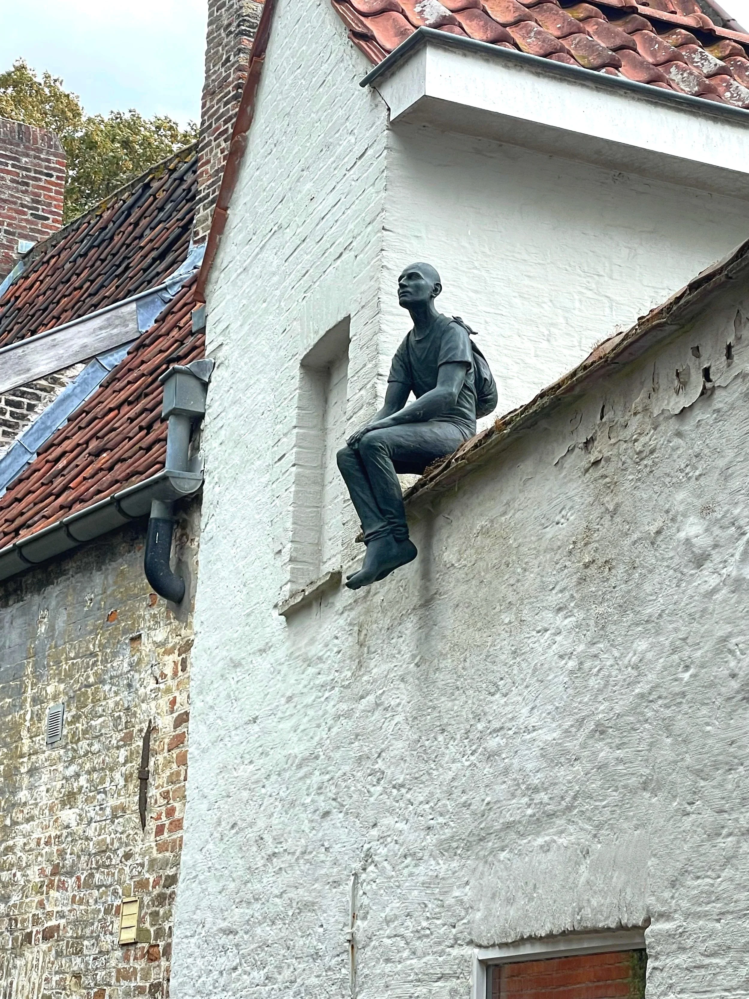A decorative statue of a young man sitting on the edge of a building's roof, with a backpack, looking into the distance.