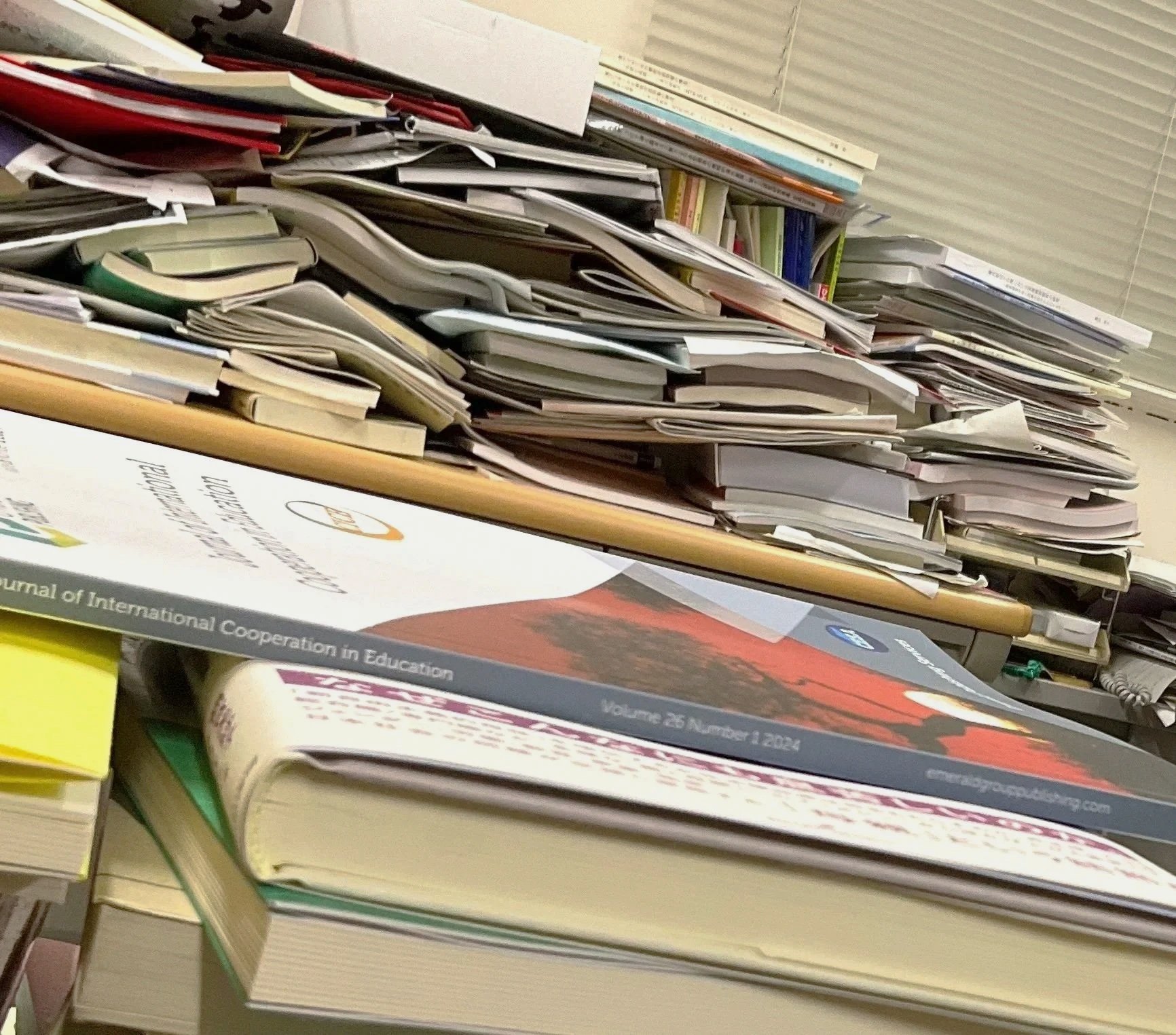 A cluttered desk with many stacked and scattered papers, notebooks, and magazines.