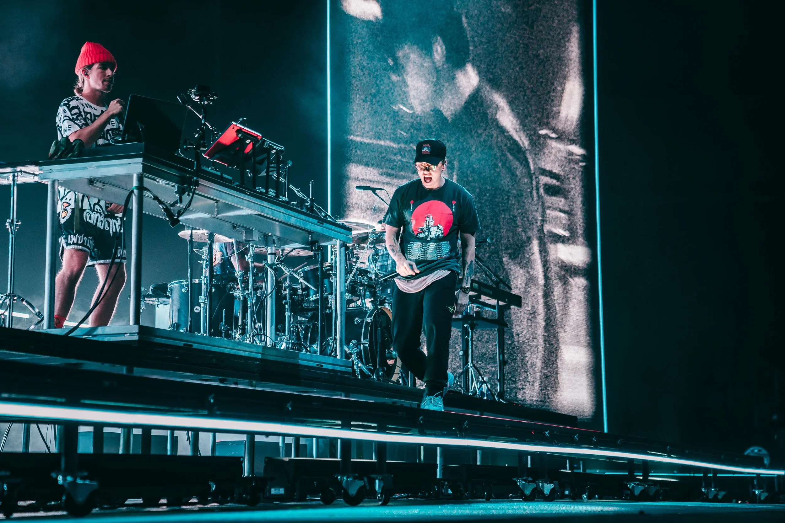 Musician LOGIC performing on stage for the Confessions of a Dangerous Mind Tour with electronic equipment and drums, illuminated by blue LED lights, during a concert. STATION SIX PRODUCTIONS.