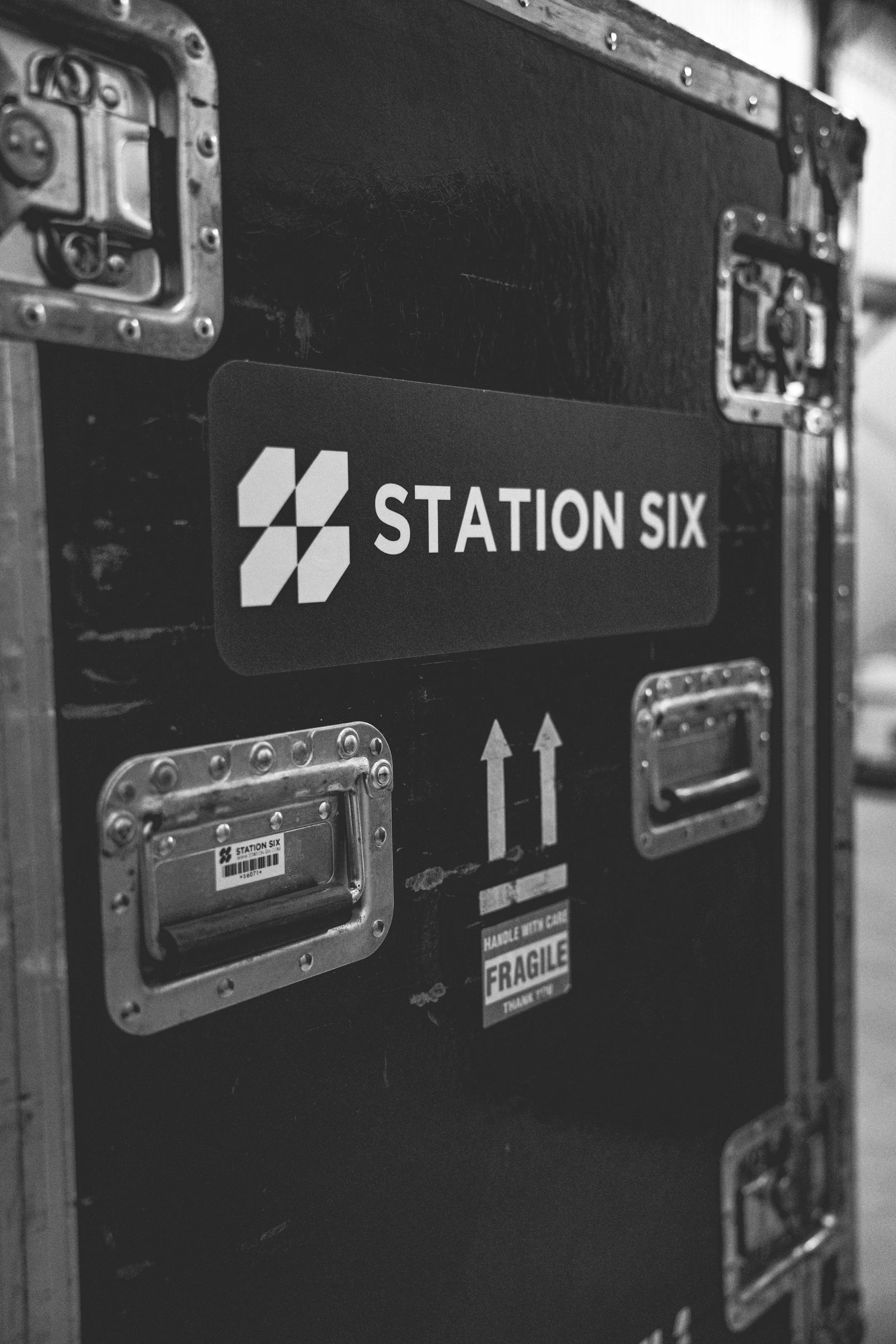 Black roadcase with metal handles, stickers, and labels including a large Station Six logo, arrows, and a fragile sticker. Concert Production, Stage Design, STATION SIX