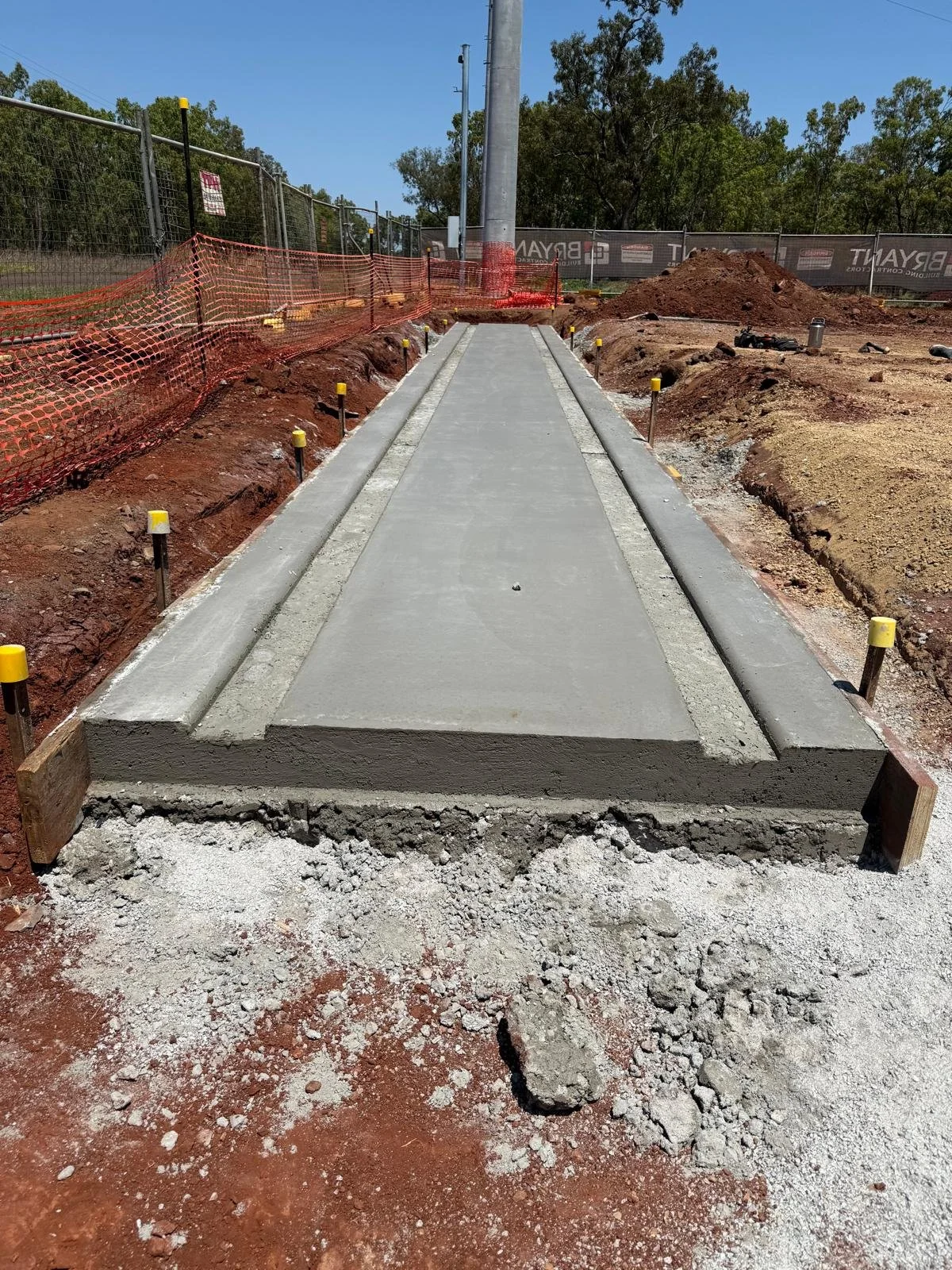 Concrete foundation slab constructed within a fenced construction site, showing fresh formwork and compacted red earth during early-stage infrastructure works.