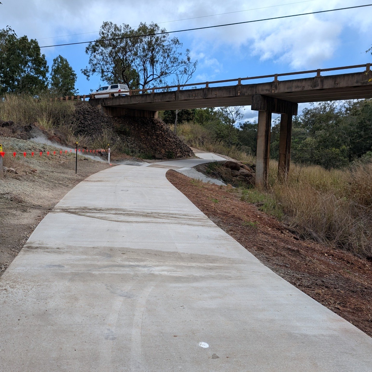 Newly constructed concrete path winding under a rural bridge at Rocky Creek Rail Trail, improving pedestrian and cyclist access in a natural bushland setting.