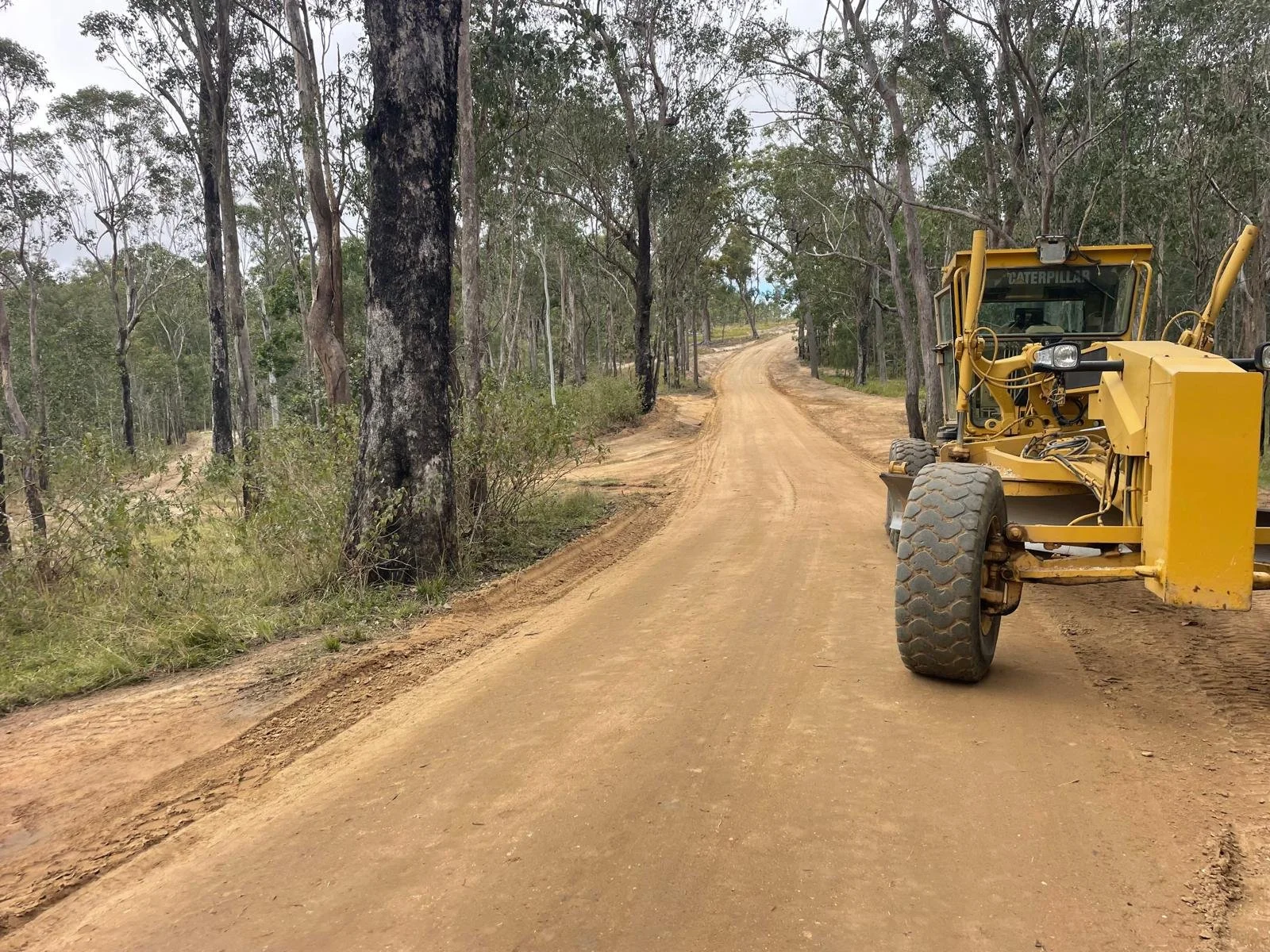 Grader working on unsealed road through open forest, showing mid-upgrade conditions along a rural stretch of Cashmere Kirrama Road in Far North Queensland.