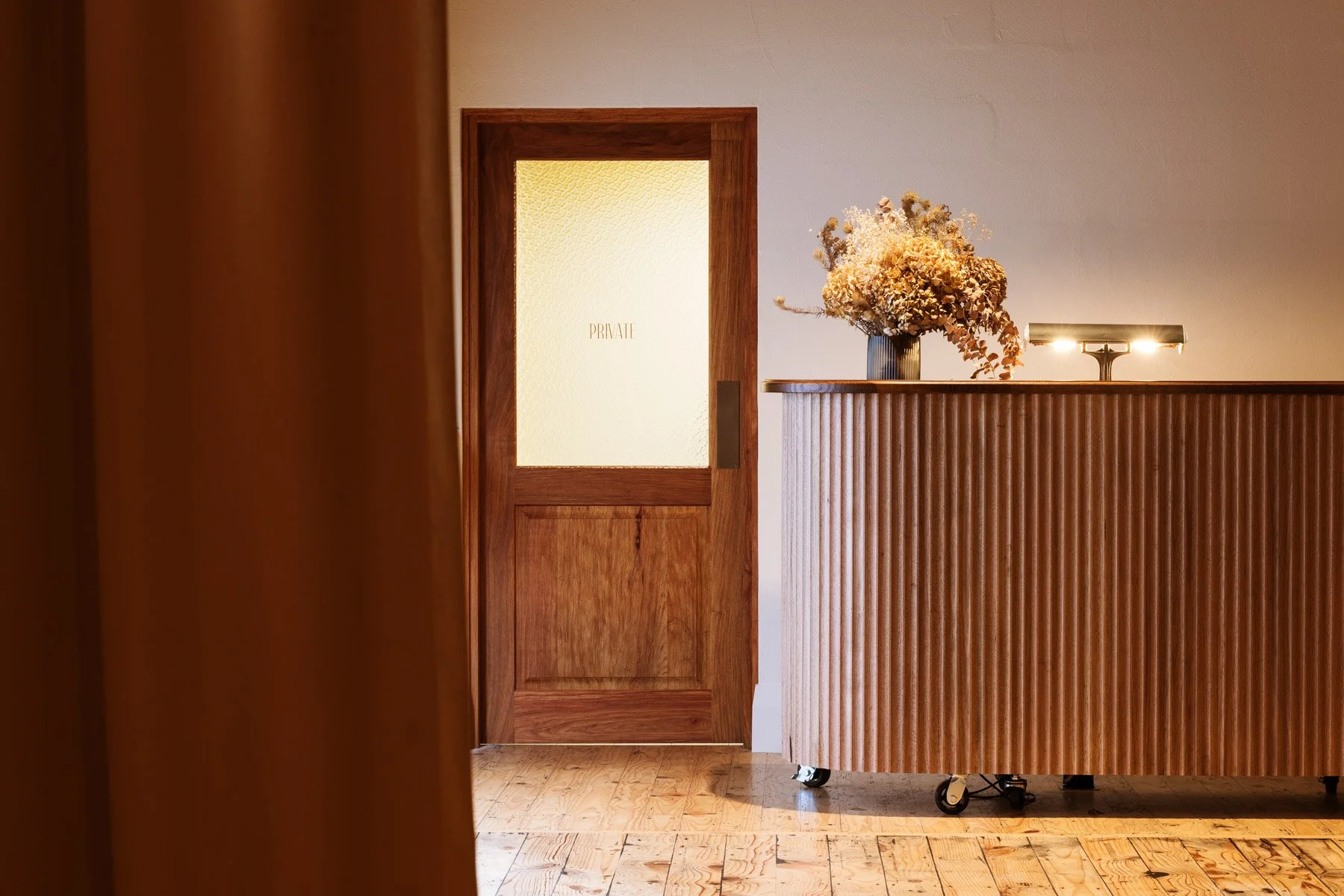 A reception area with a wooden counter, a vase of dried flowers, and a door labeled 'PRIVATE' in the background.