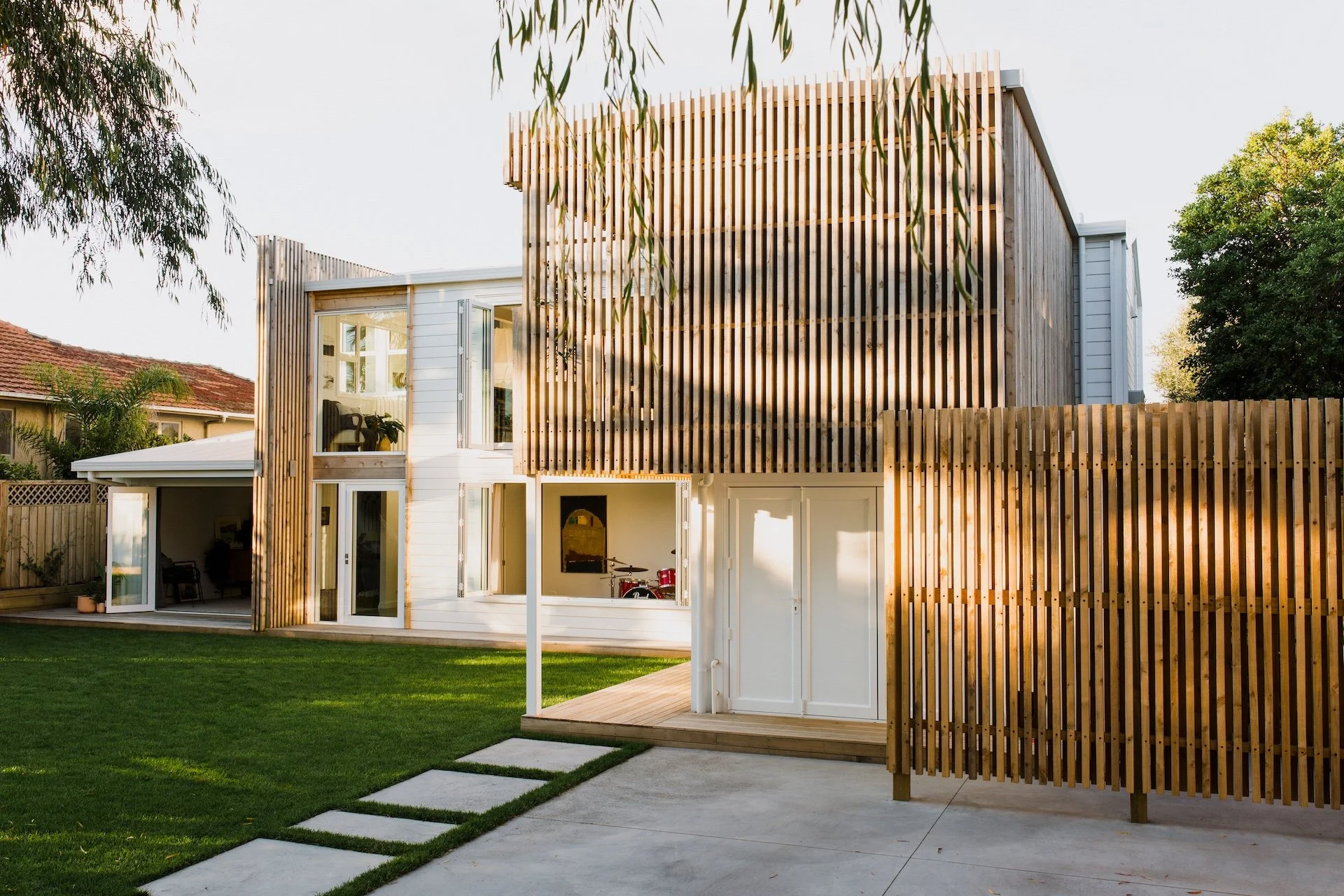 Modern two-story house with white and wooden exterior, large windows, a backyard lawn, and a wooden fence.