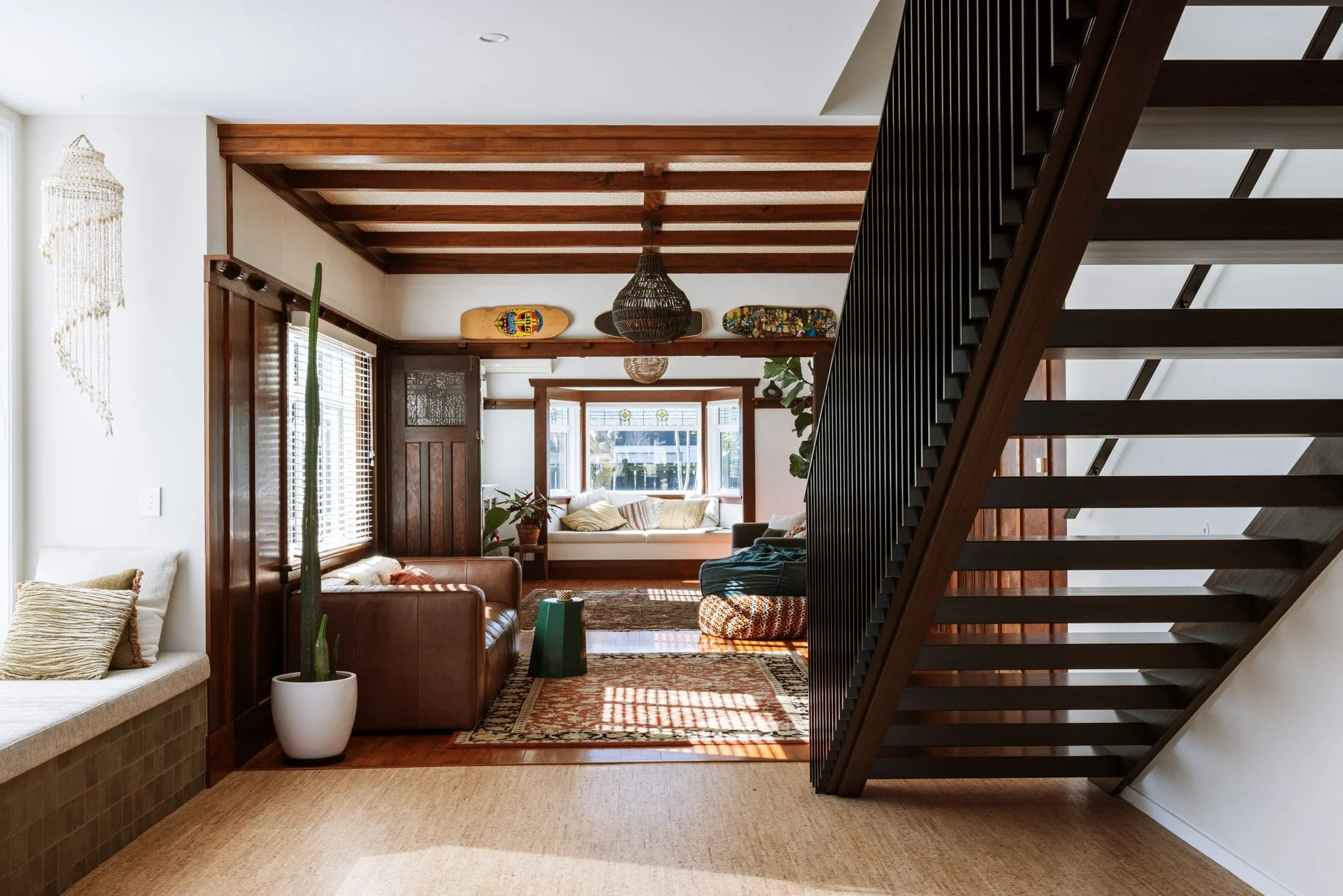 Interior view of a living room with wooden accents, a staircase on the right, and a window seat in the back with cushions.