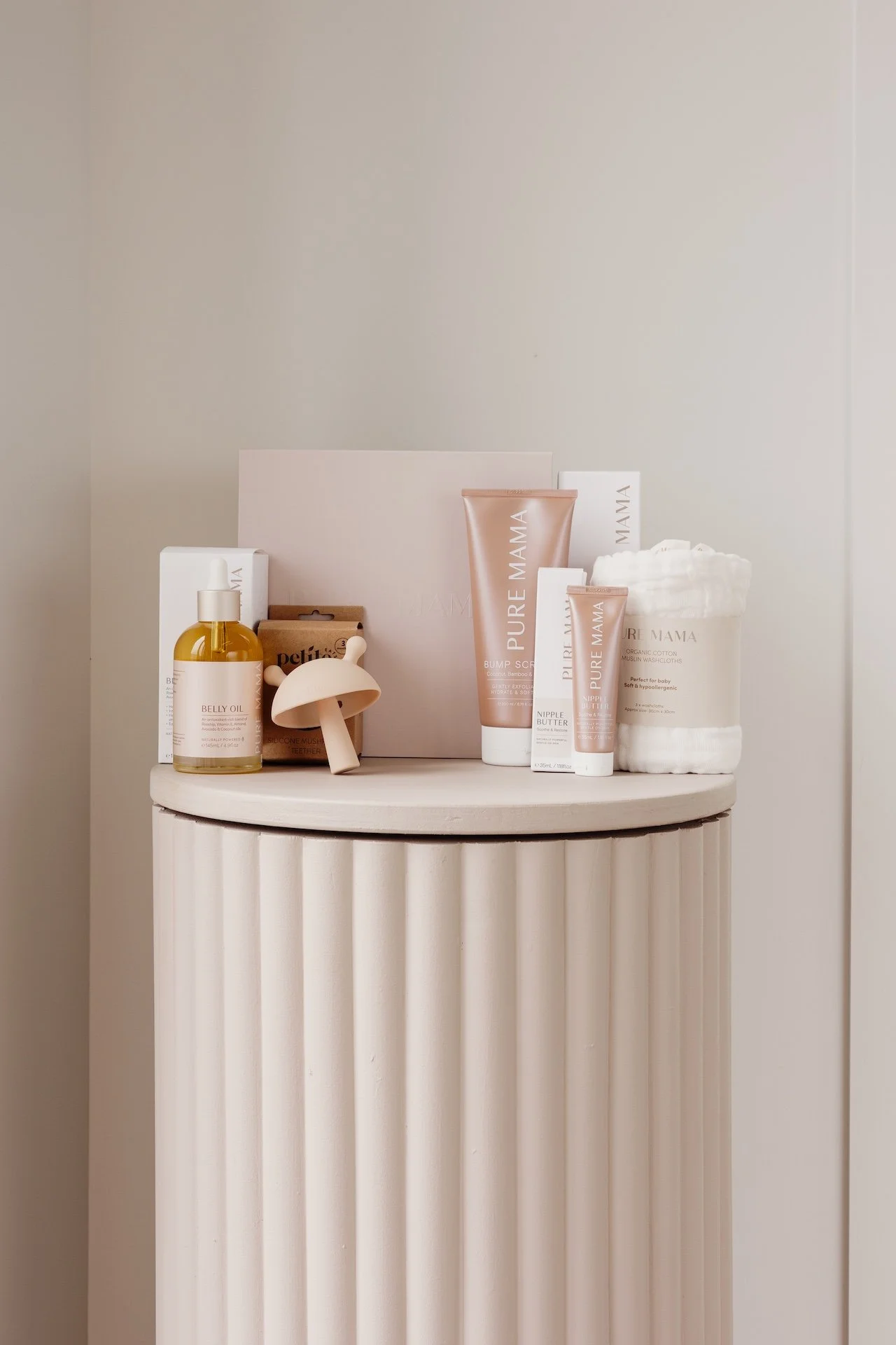 Collection of skincare and body care products on a white fluted pedestal, including oil, creams, and a towel. Commercial lifestyle product photography in Papamoa.