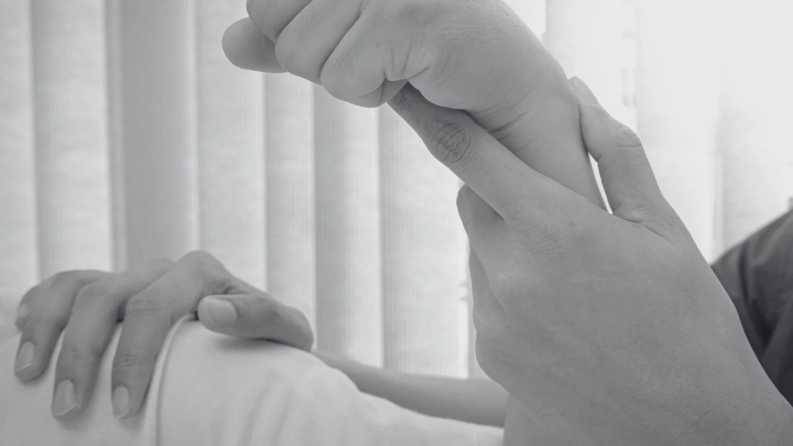 A grayscale image showing a close-up of a patient's hand, a physical therapist helping correct pain in a patient's wrist.