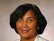 A woman with dark hair, wearing what looks like a lab coat
