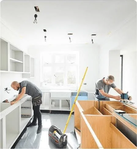 Two people installing kitchen cabinets in a bright, white kitchen.
