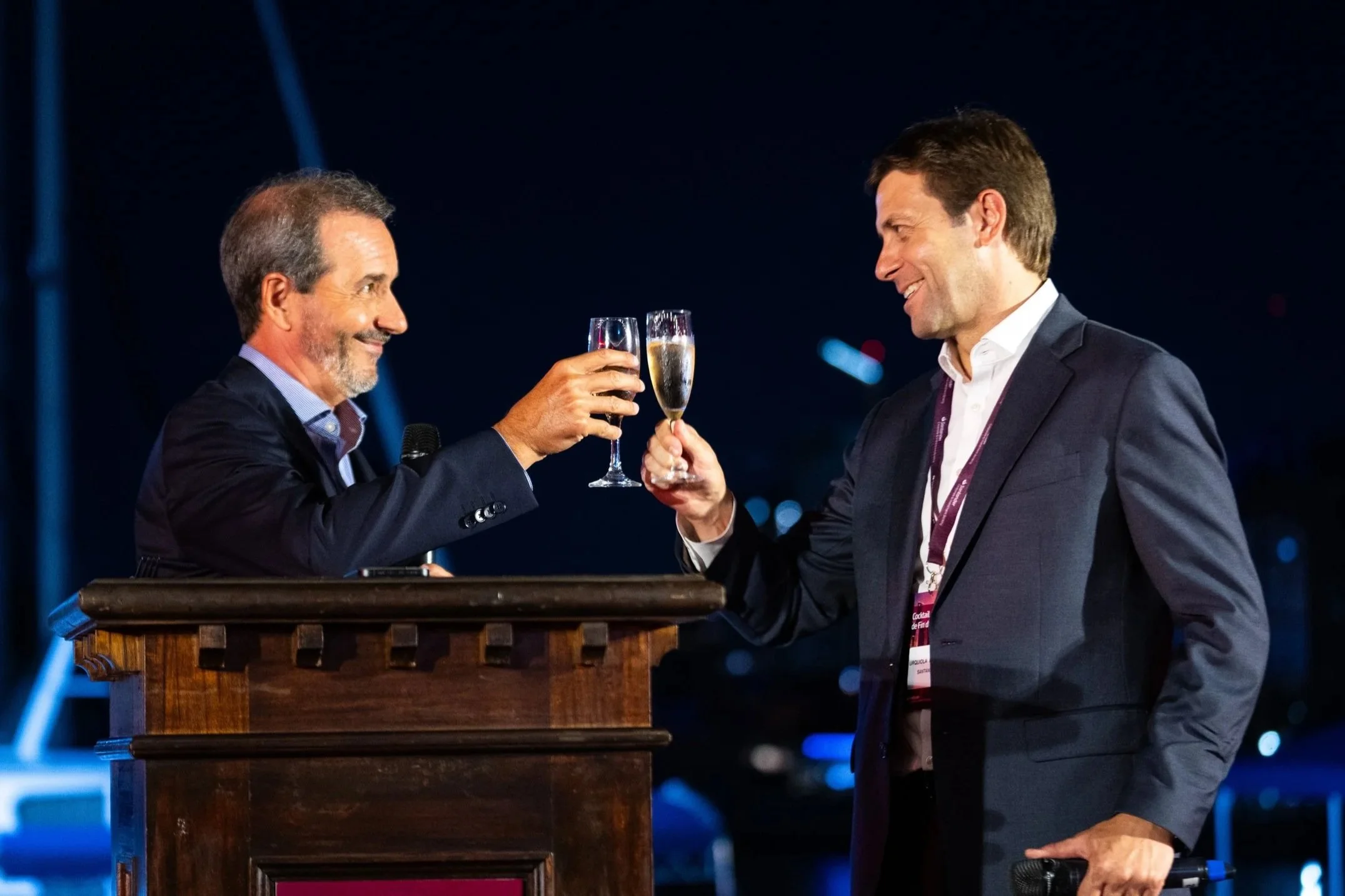 Dos hombres de negocios con trajes brindan con copas de champagne en un evento nocturno.