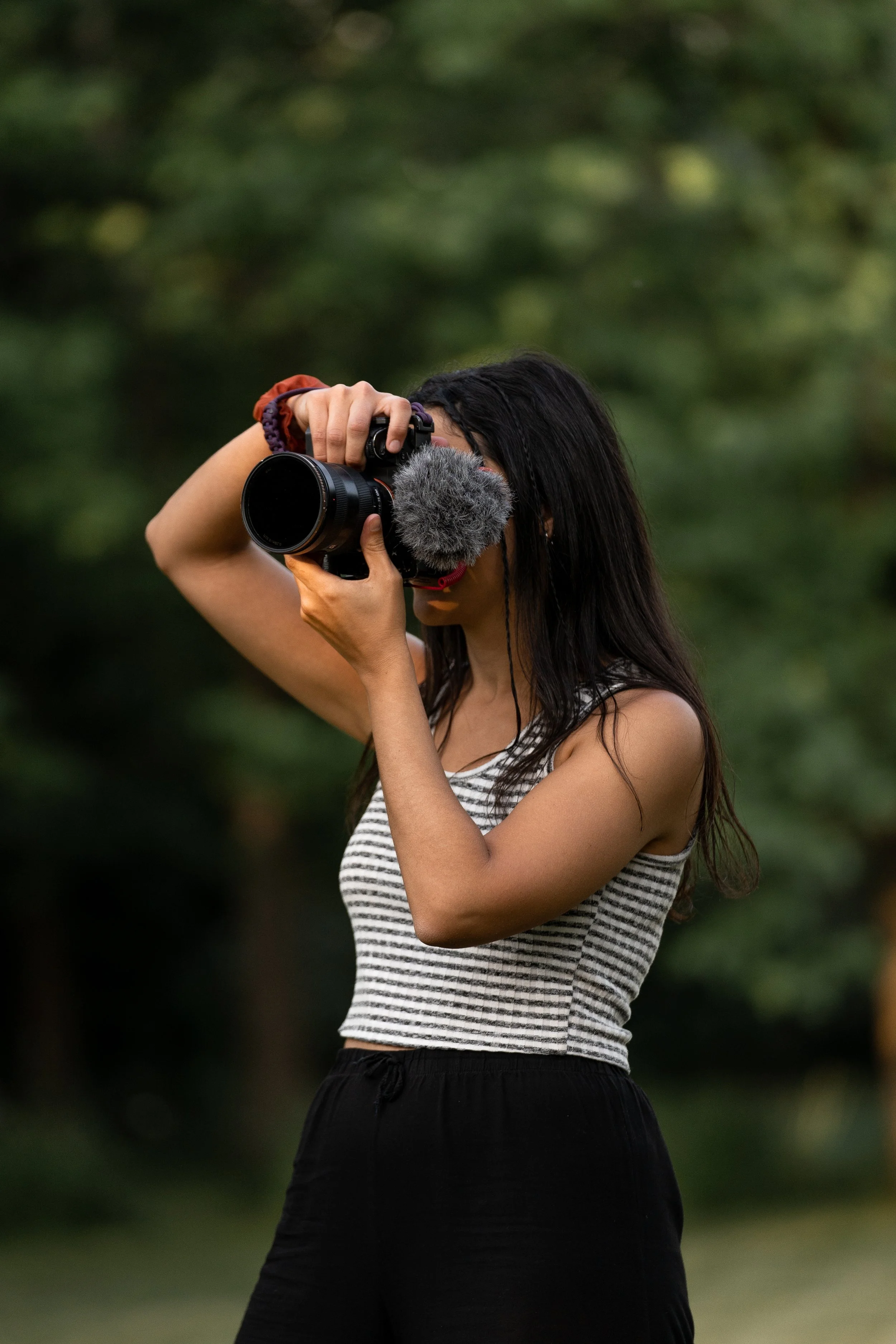 Una mujer joven tomando una fotografía con una cámara en un entorno natural con árboles verdeados.