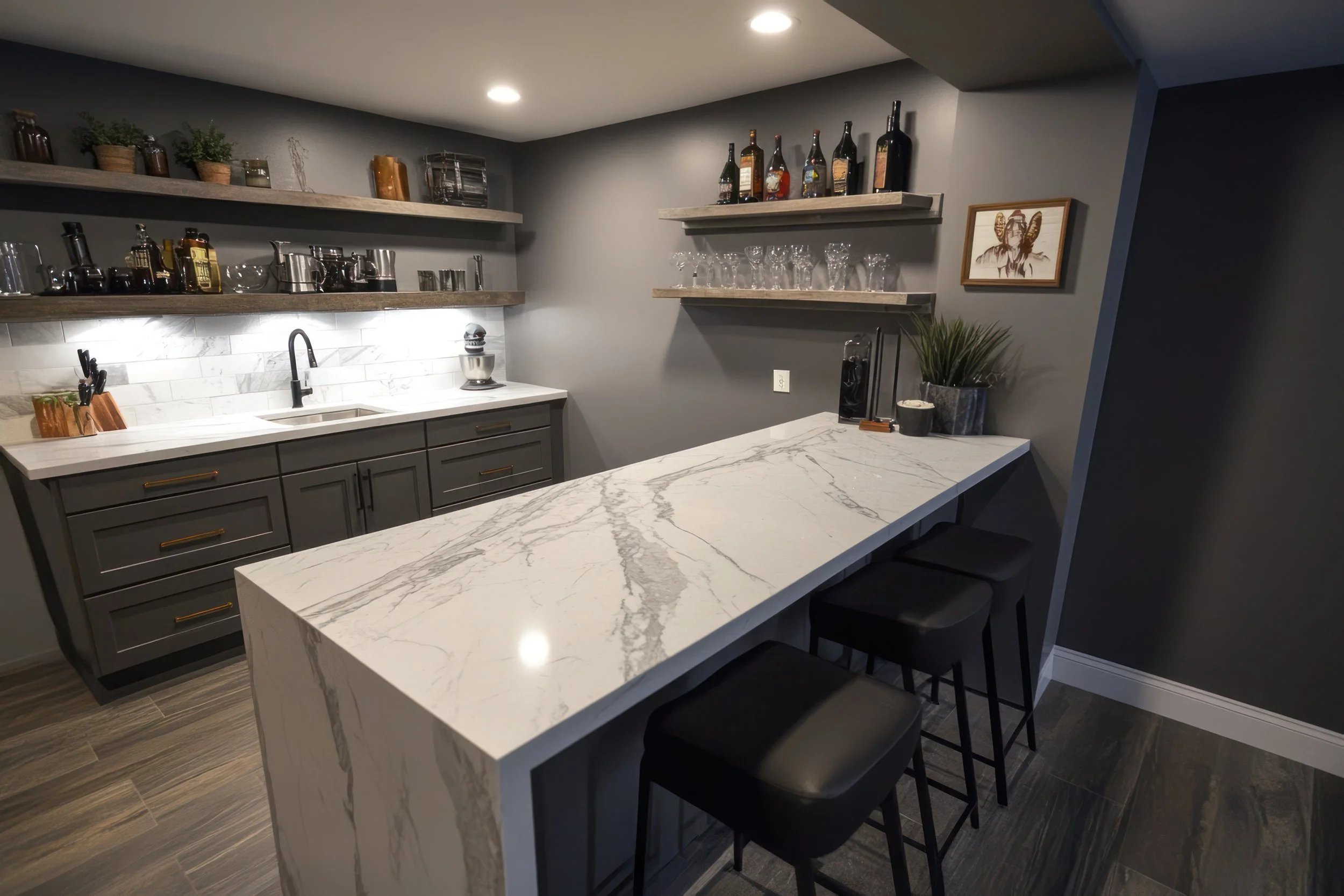 Modern kitchen with marble island, gray cabinets, open shelves with bottles and glasses, and gray walls.