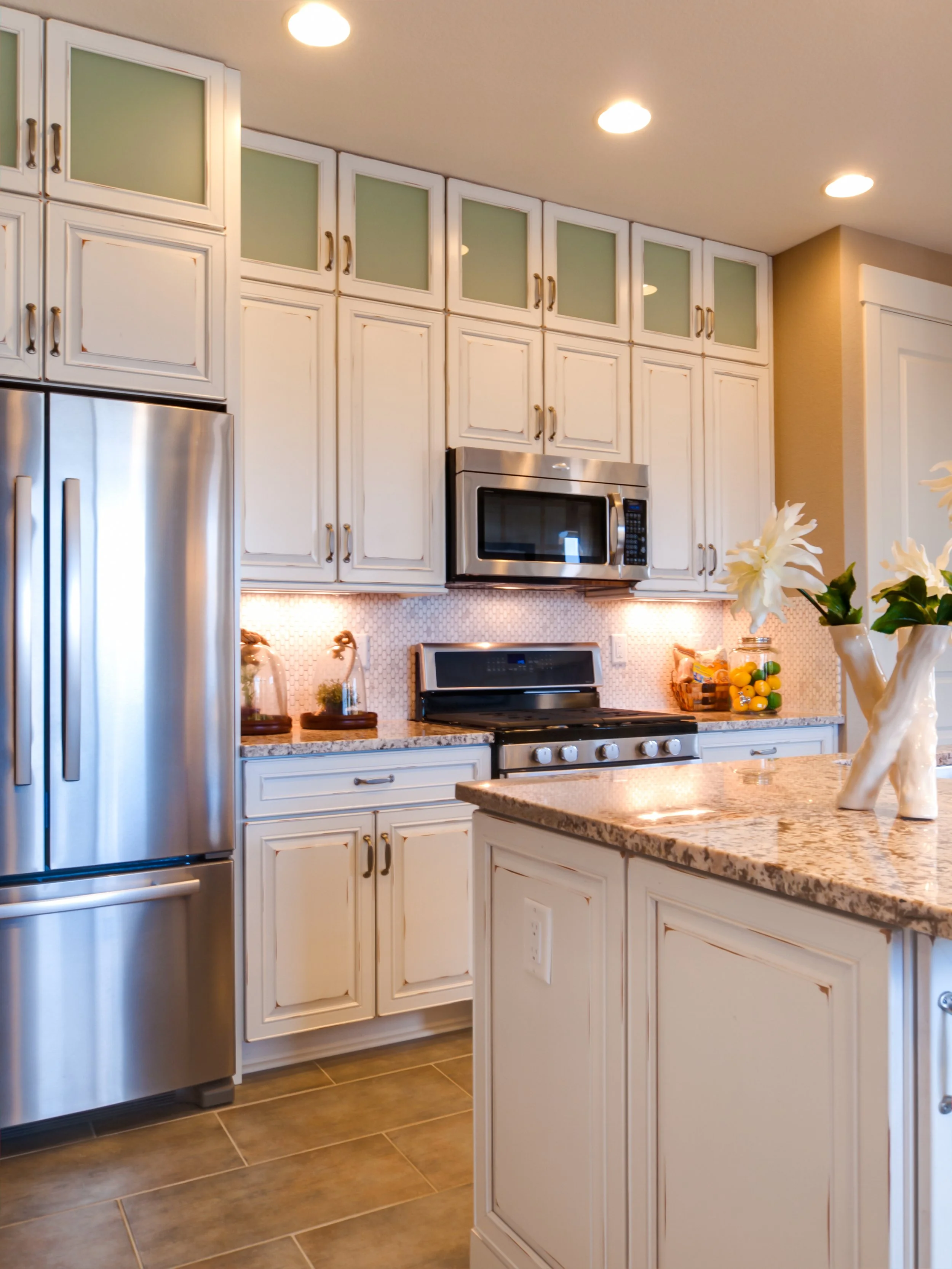 Kitchen with white cabinets, stainless steel appliances, and a granite countertop featuring a vase with white flowers and a basket of lemons.