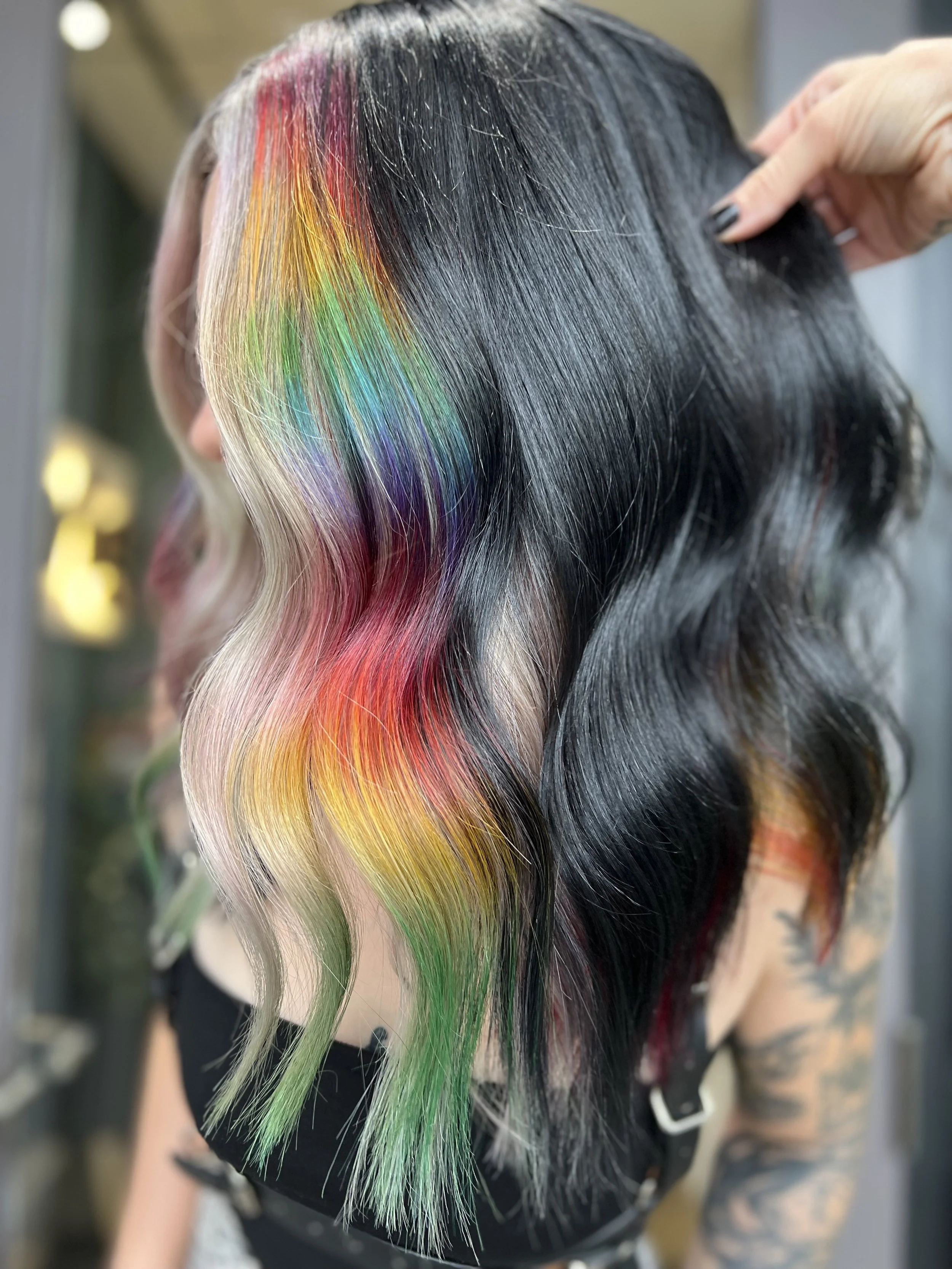 Hair with black base color and rainbow-colored streaks, styled in loose waves.
