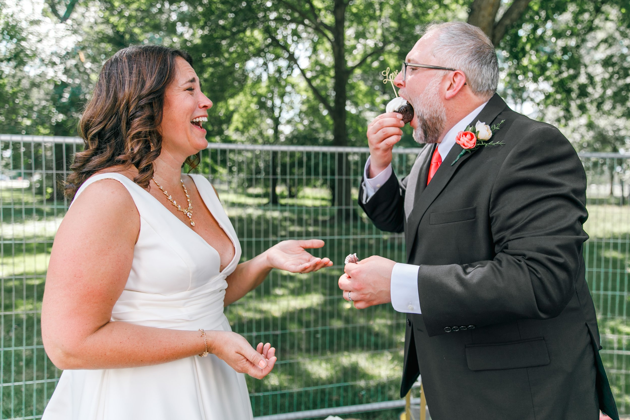 A bride laughing as her new husband shoves a cupcake in his mouth after their elopement at the DC War Memorial in Washington DC.