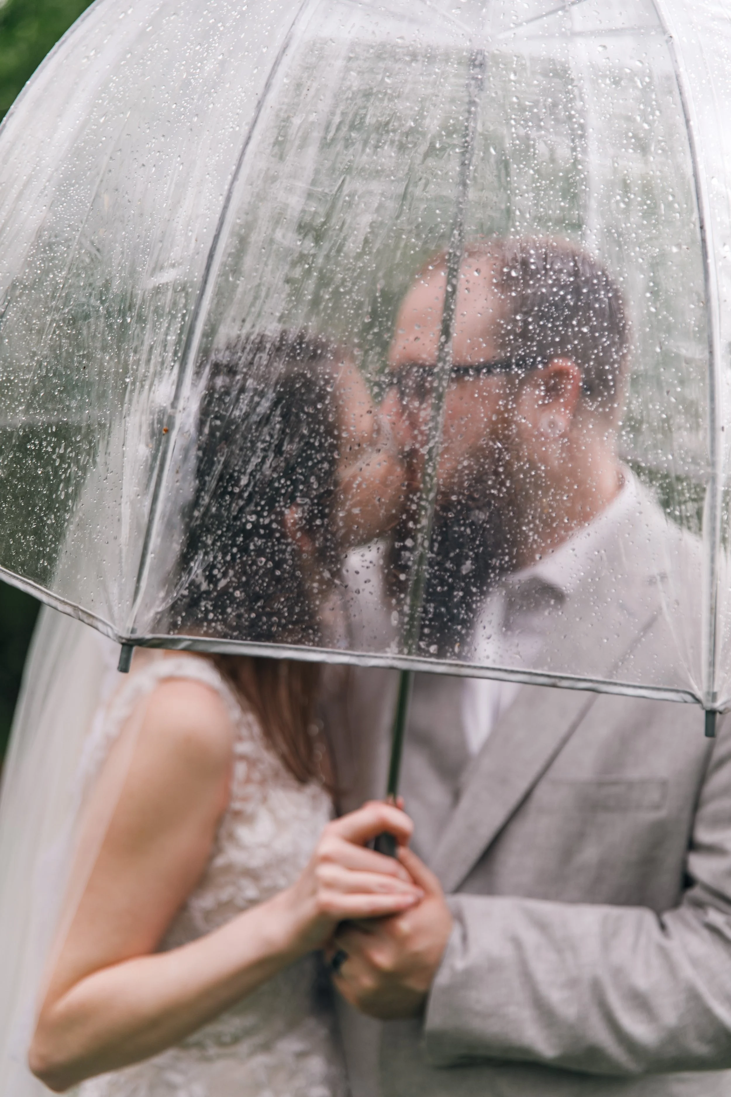 A romantic couple shares a kiss under a transparent umbrella on a rainy day.