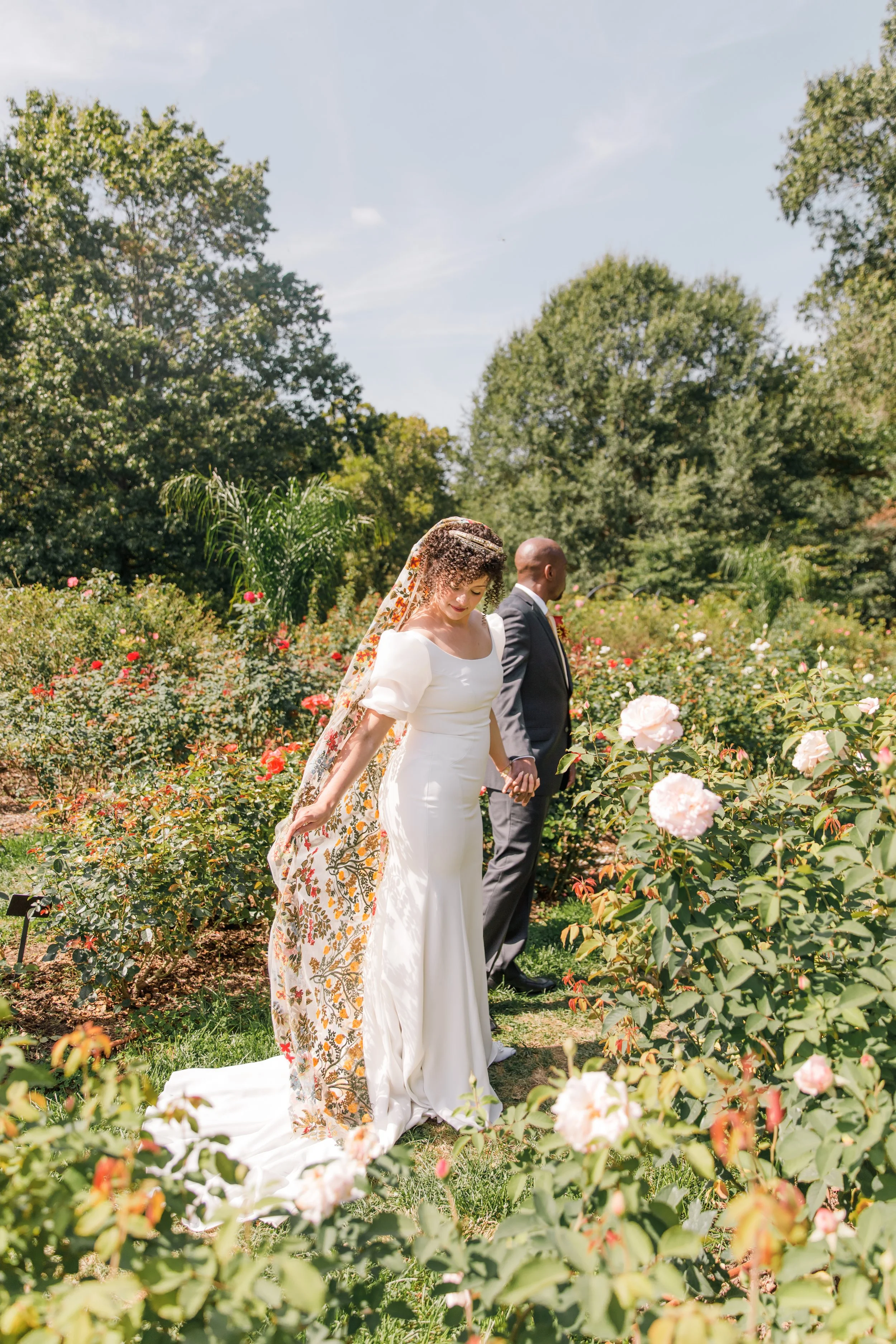 A bride fluffing her veil while being led through the Bon Air Rose Garden before their elopement in Virginia.