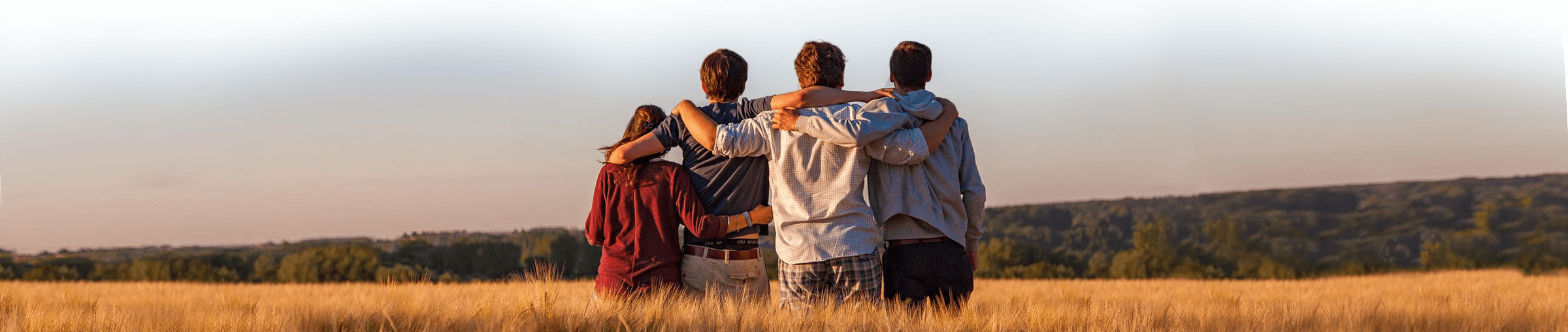 four people in a field looking away with their arms around each other