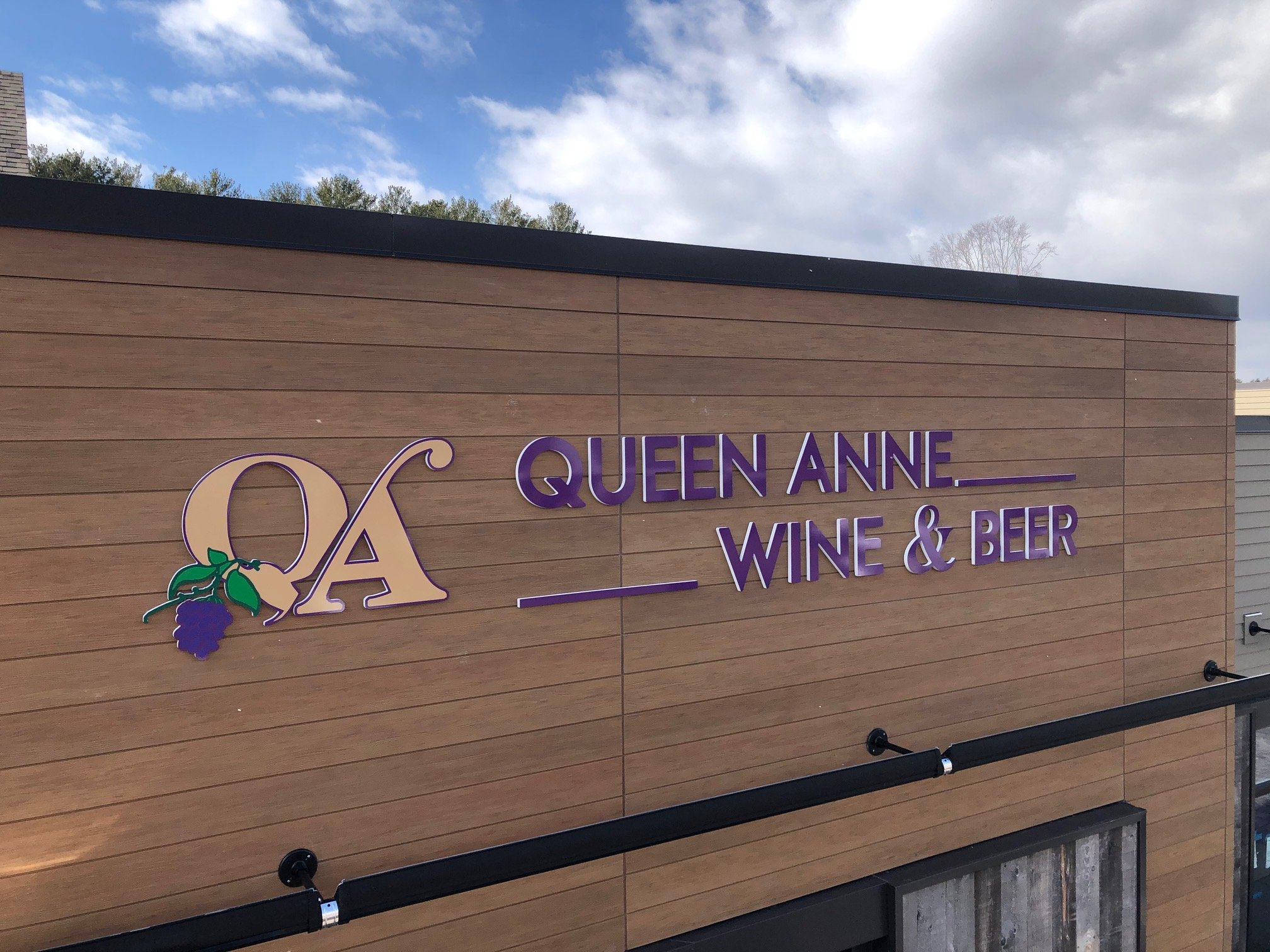 Stunning lettering on storefront sign for Queen Anne Wine & Beer with a grape cluster and a stylized logo on a wooden wall.