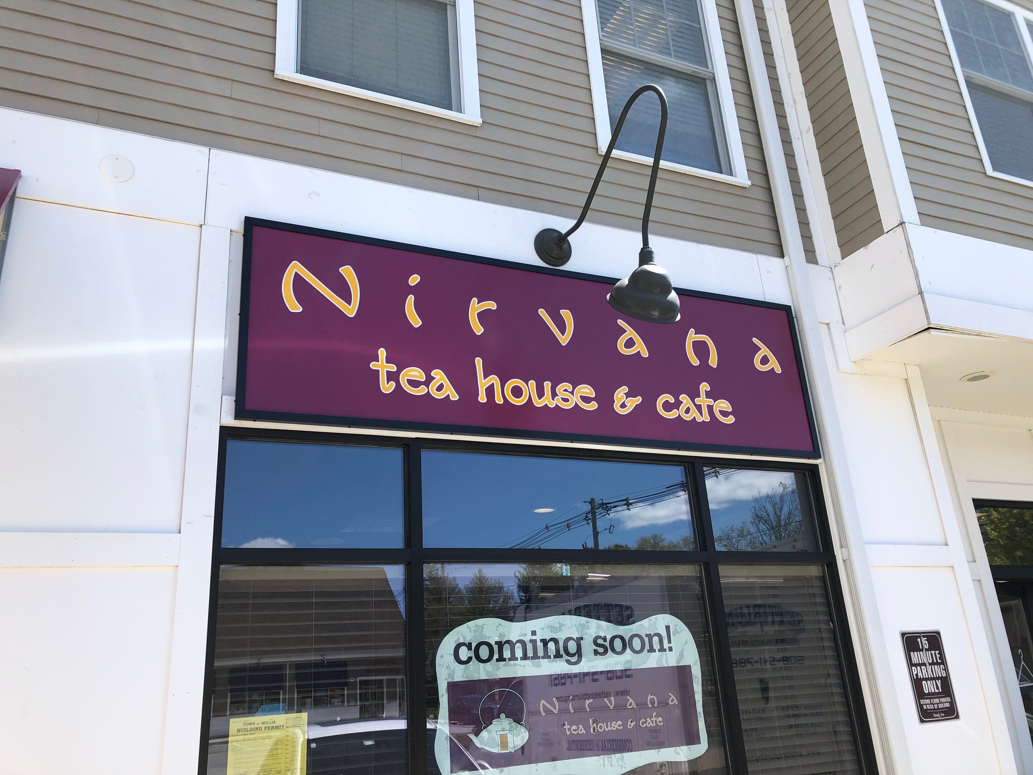 Stylized sign for Nirvana Tea House & Cafe with a 'coming soon!' window sign in front of a building with windows.