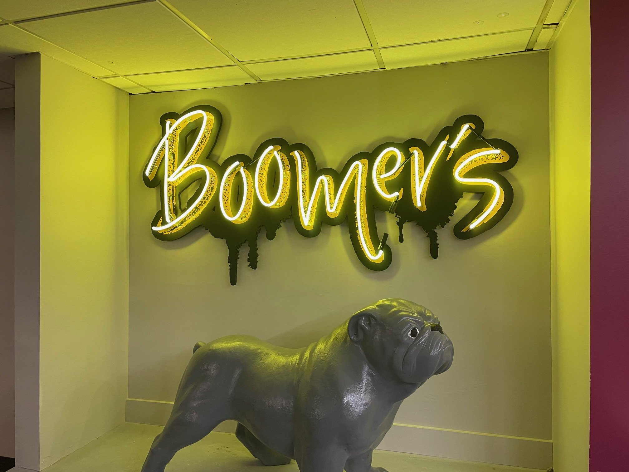 Neon sign that reads 'Bowie's' above a sculpture of a dog inside a room with yellow and pink walls.