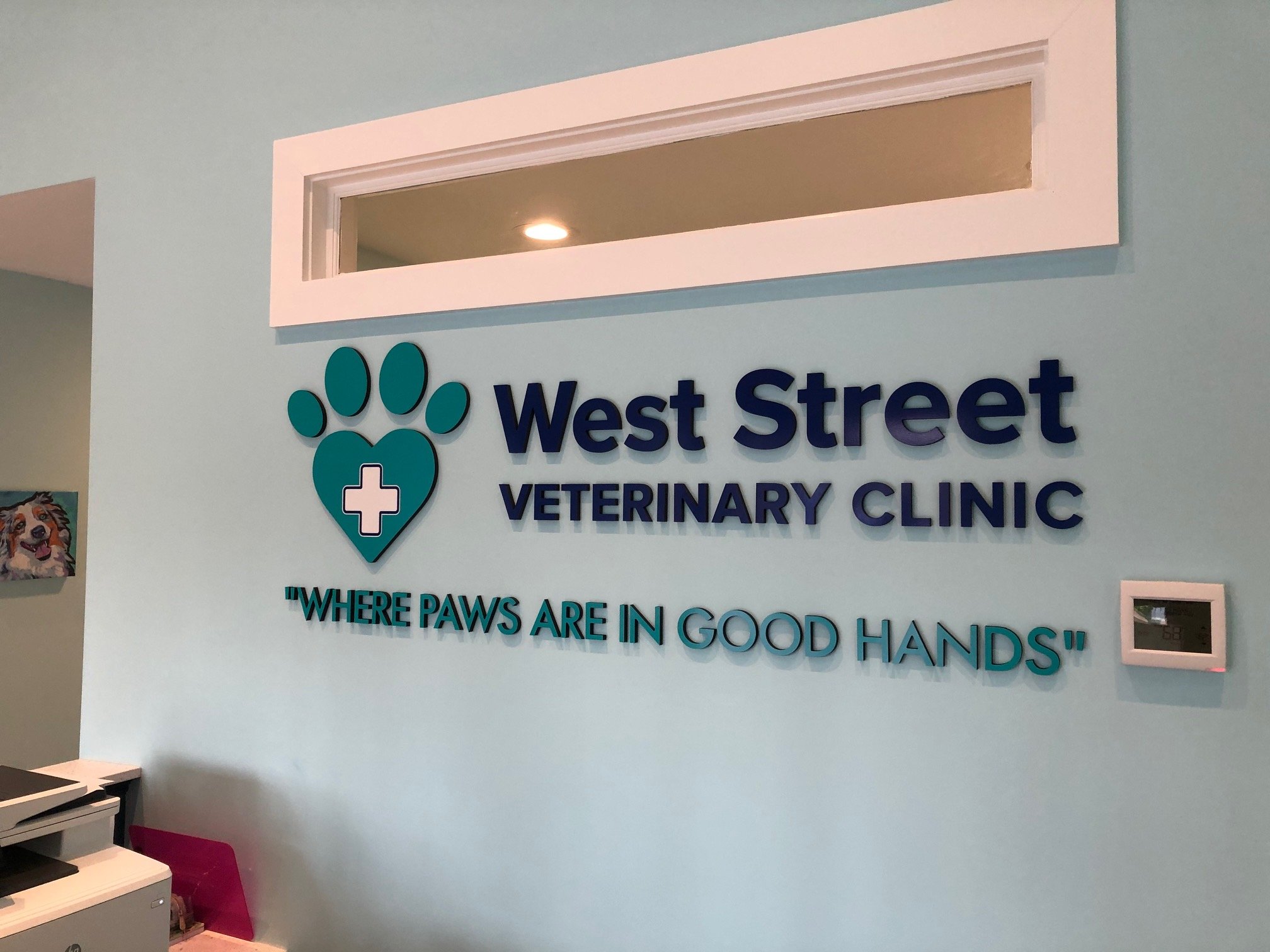 Sign for West Street Veterinary Clinic including logo of a paw print with a cross inside, and the slogan 'Where Paws Are In Good Hands' on a light blue wall.