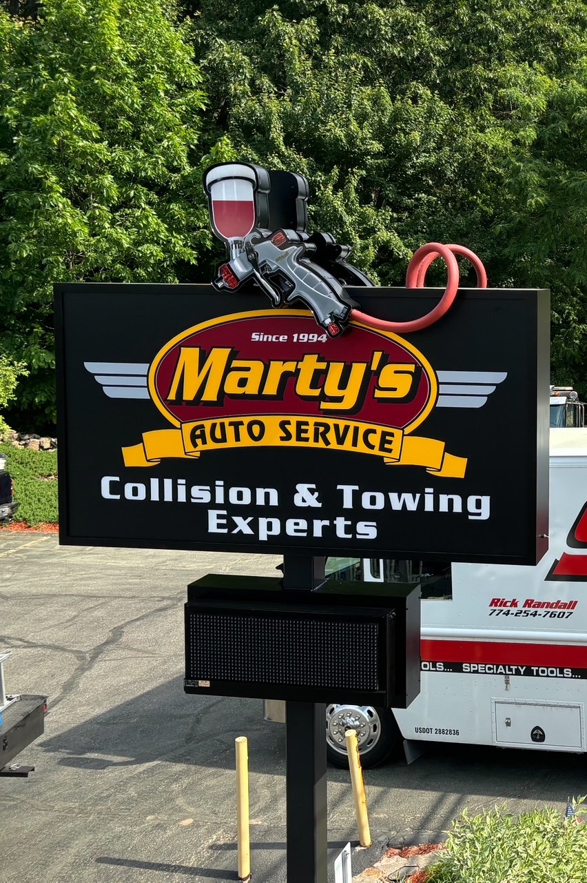 Large freestanding digital sign for Marty’s Auto Service with a cartoon air impact wrench and tire gauge on top, advertising collision and towing experts since 1994.