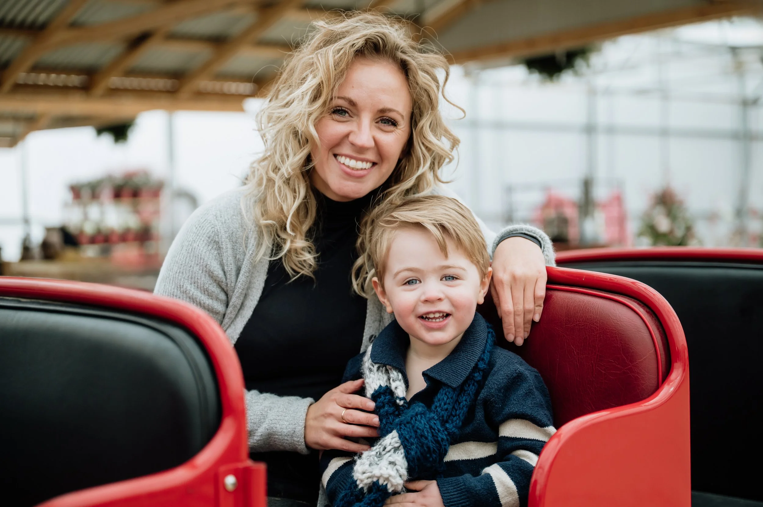 A woman and a young boy sitting together in a red amusement park ride, smiling at the camera.