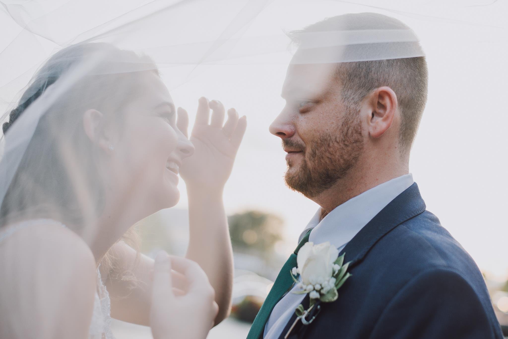 A bride and groom sharing a happy moment outdoors, close-up portrait, soft sunlight, romantic atmosphere.