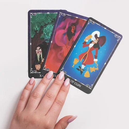 A product image composite of three tarot cards held in a person's hand, featuring a witch, a dark figure with red and pink shades, and a pirate with a sword and hat, all Disney characters.