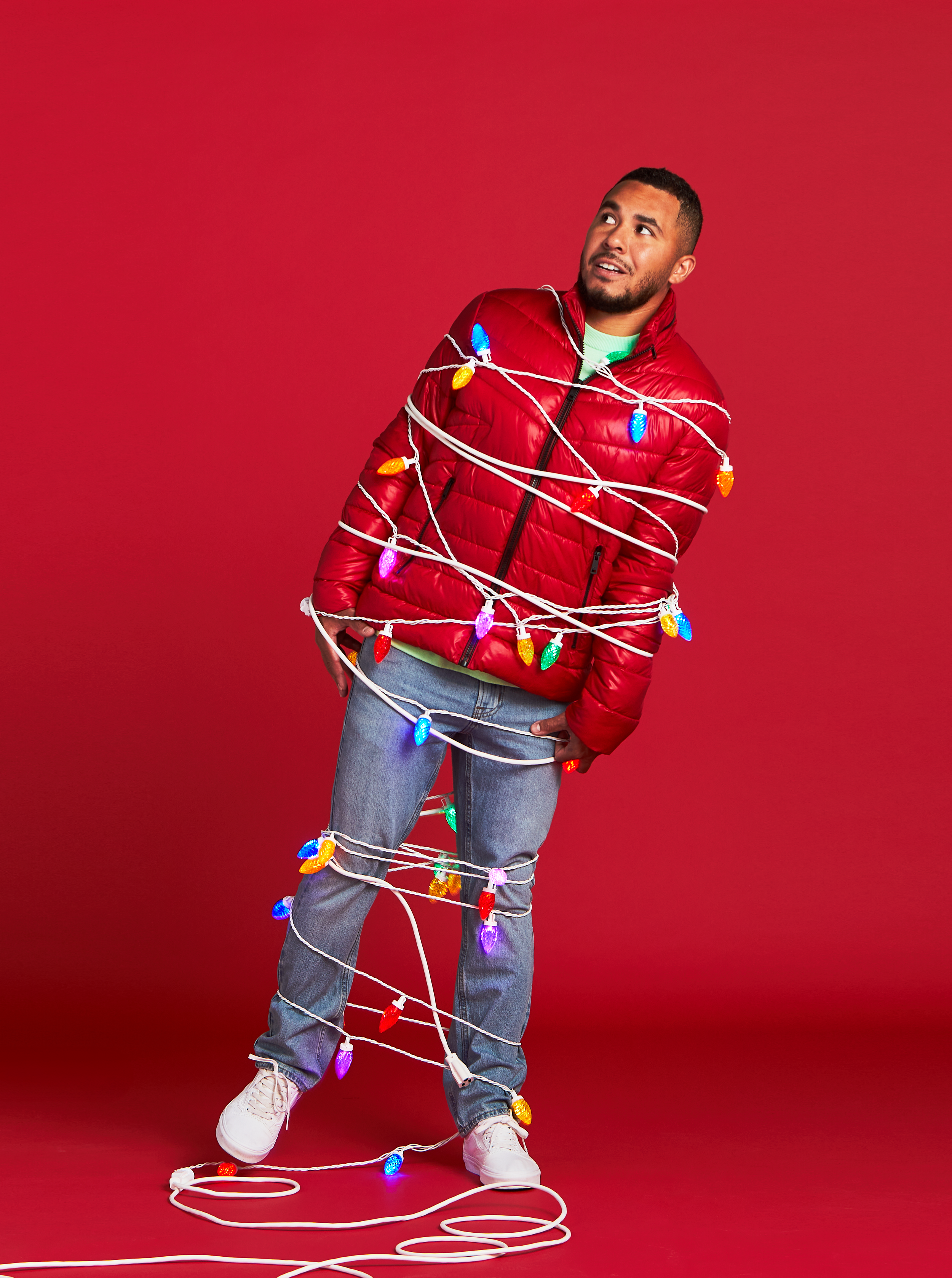 A man wrapped in colorful Christmas lights standing on a red background.