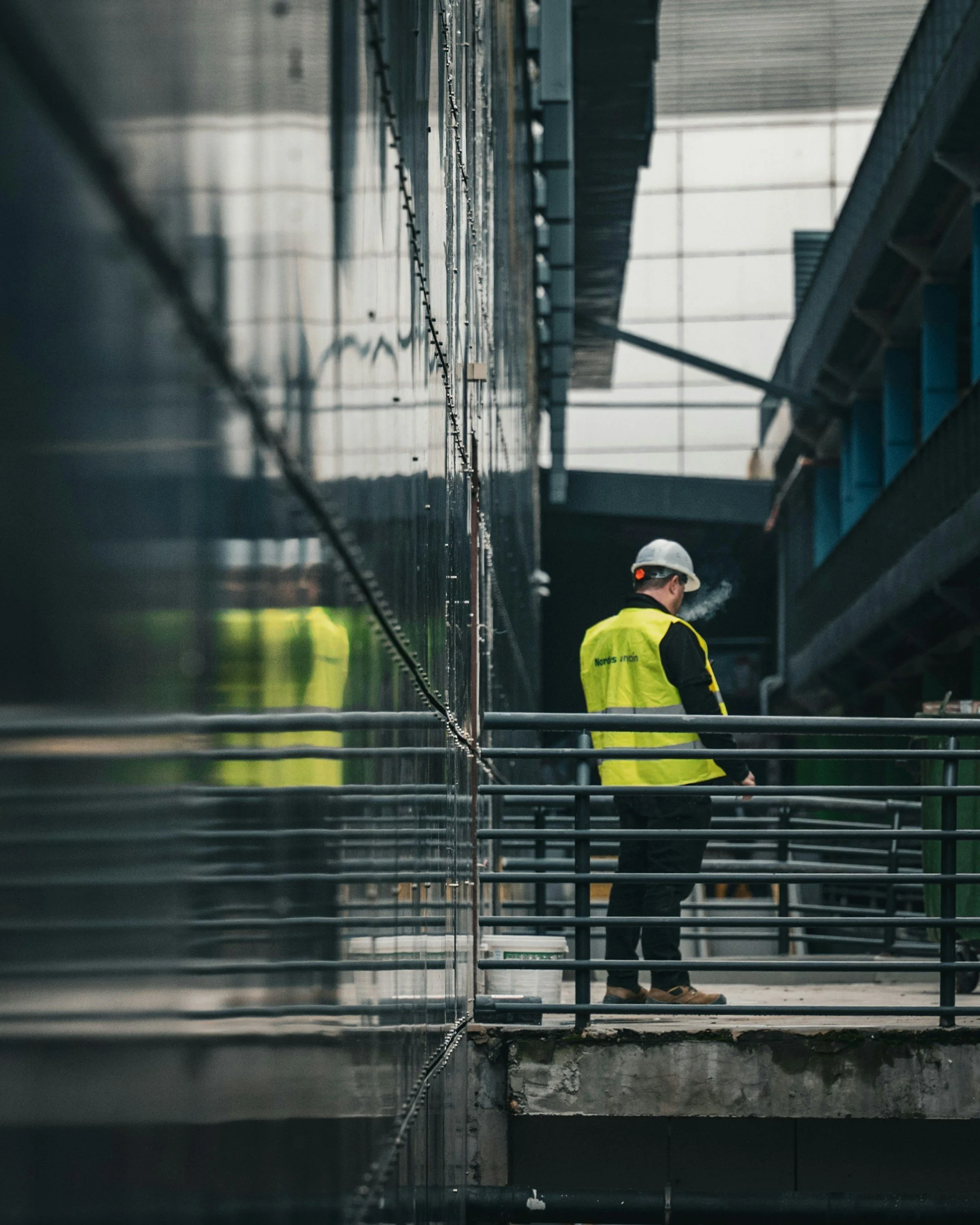 Photo of a construction worker wearing a yellow safety vest and white helmet, working on a construction site with scaffolding and building materials.