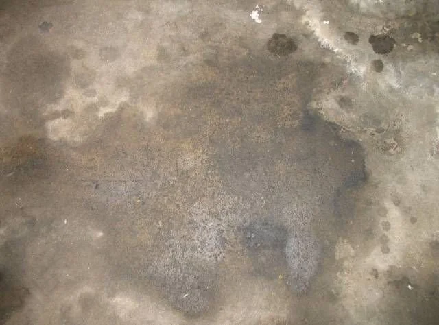 Concrete floor with a large, irregular dark stain and multiple smaller stains.
